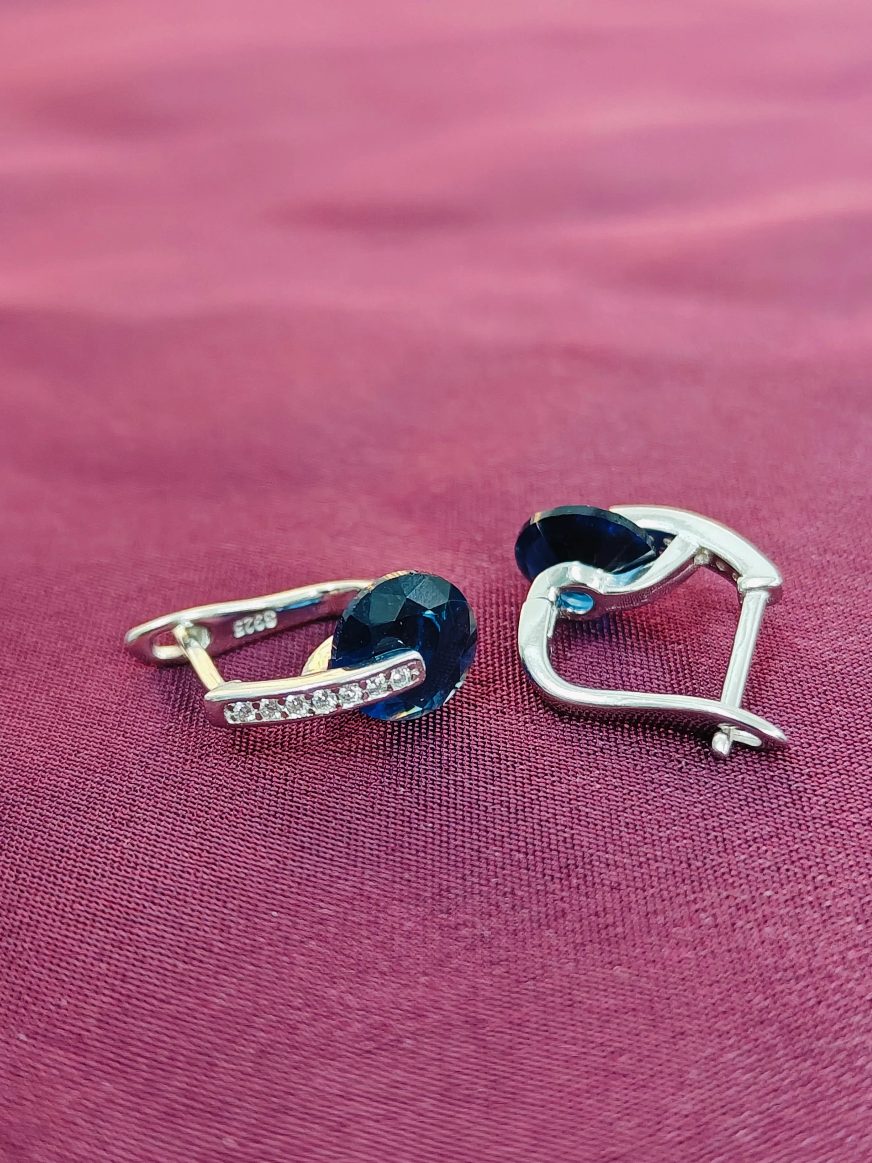 Pair of heart-shaped earrings with blue gemstones on a pink fabric background