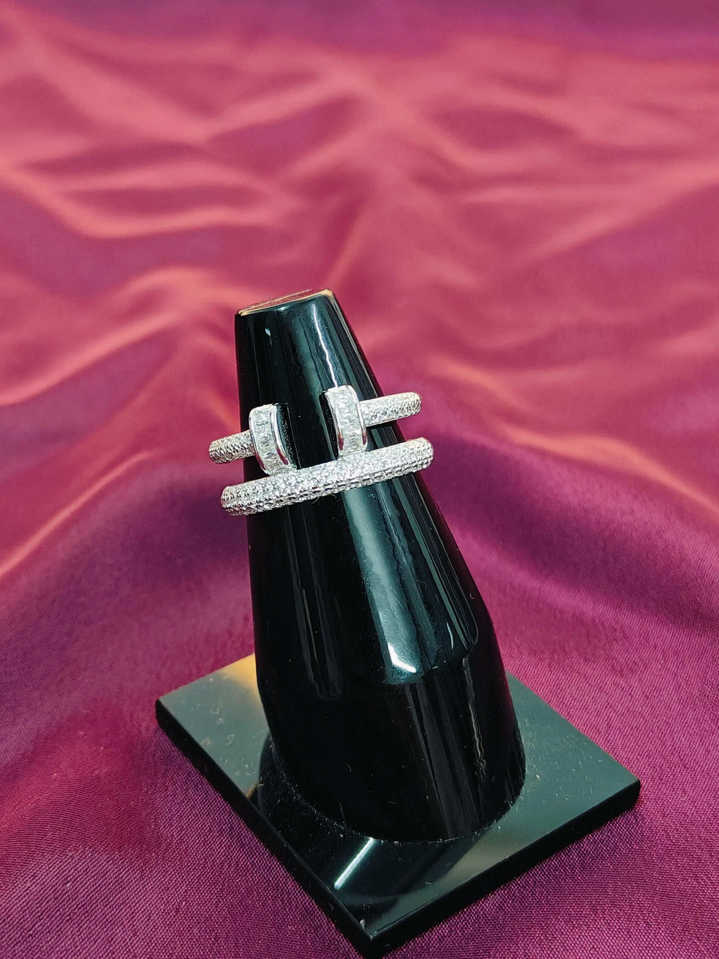 Two diamond rings on a black stand against a purple fabric background