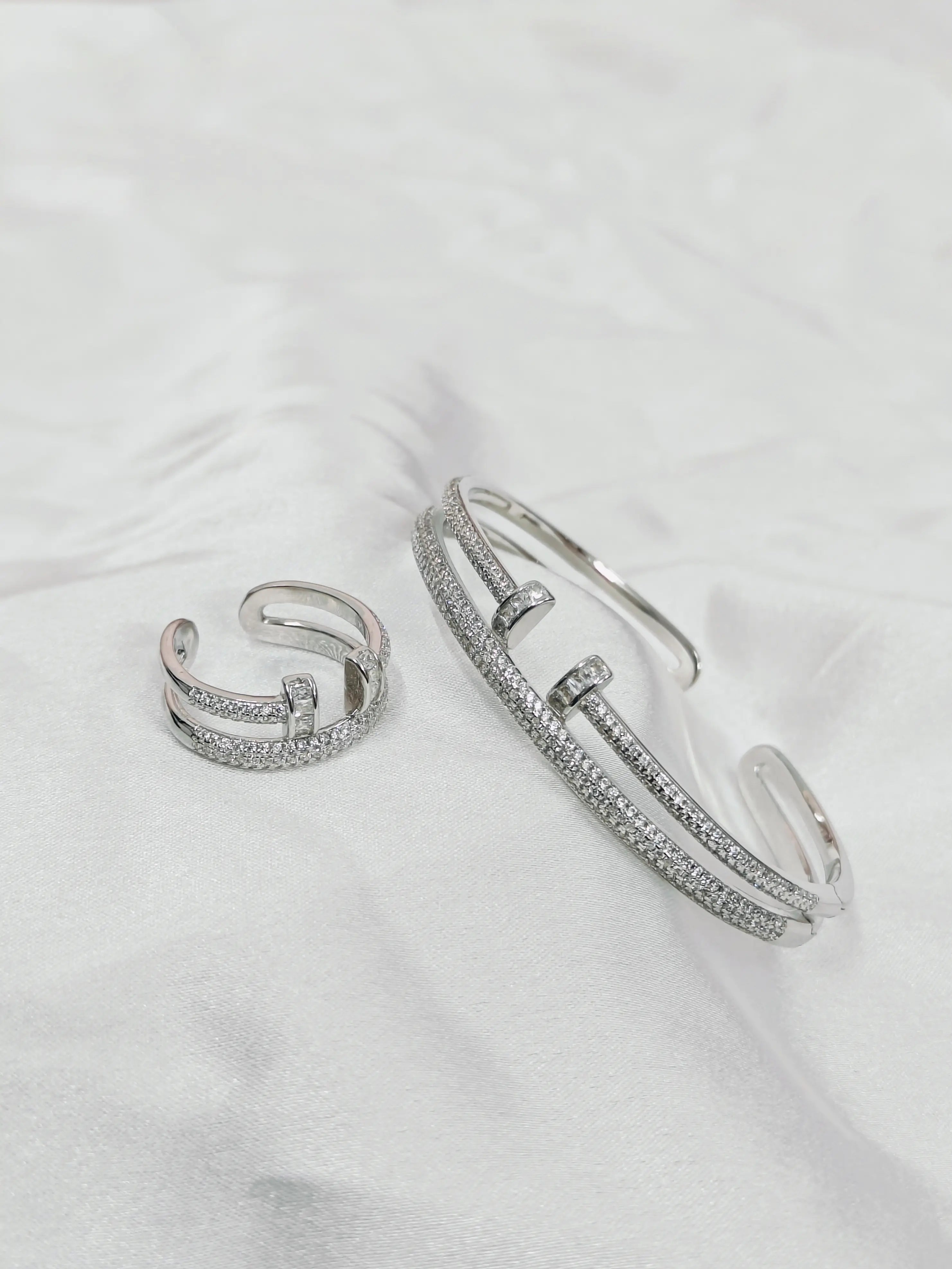Silver bracelet and ring set on a white fabric background