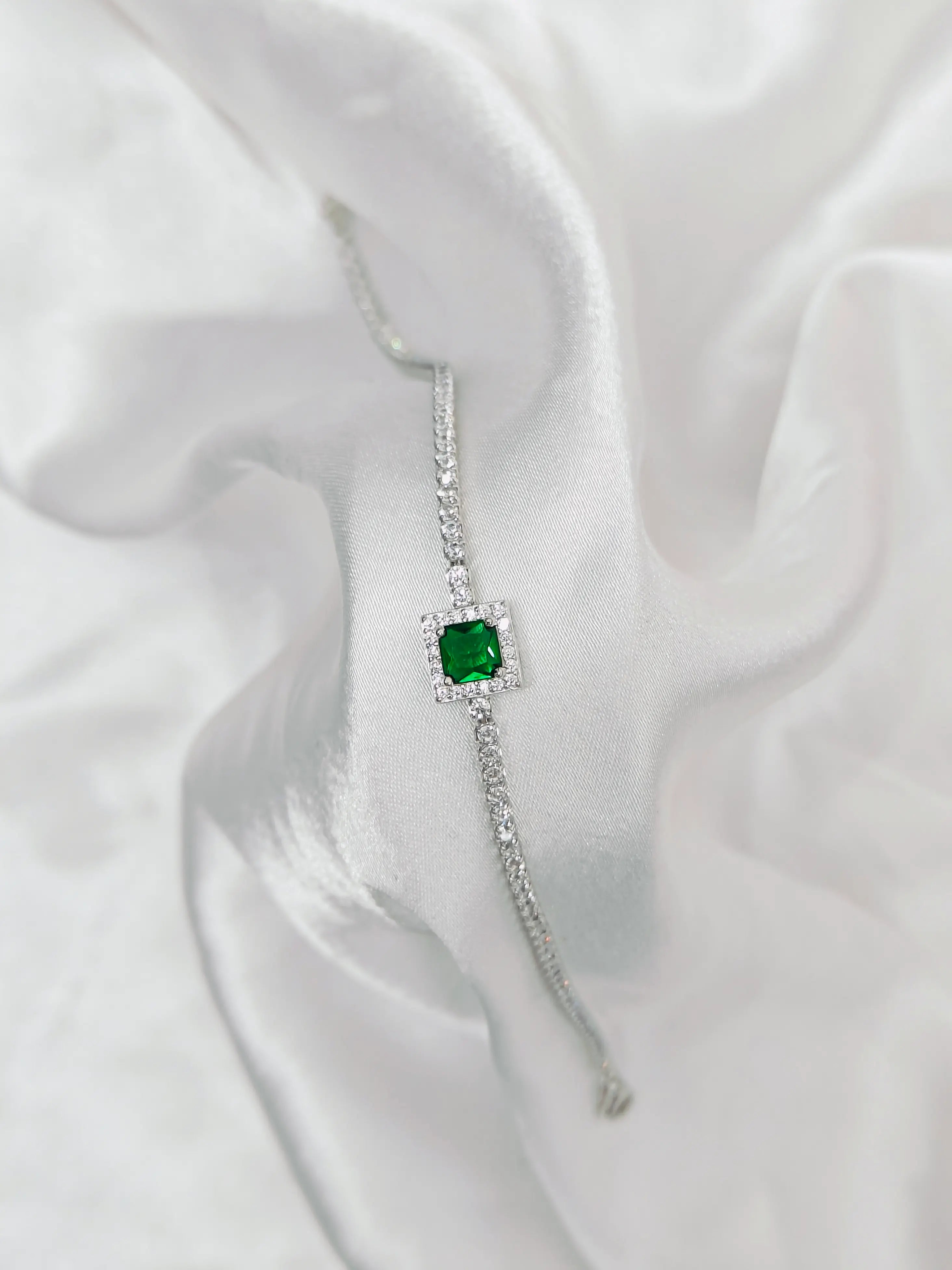 Silver bracelet with a green gemstone on a white fabric background
