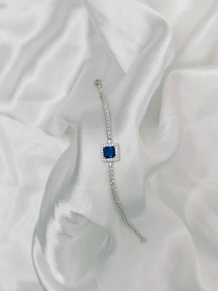 Silver bracelet with a blue gemstone on a white fabric background