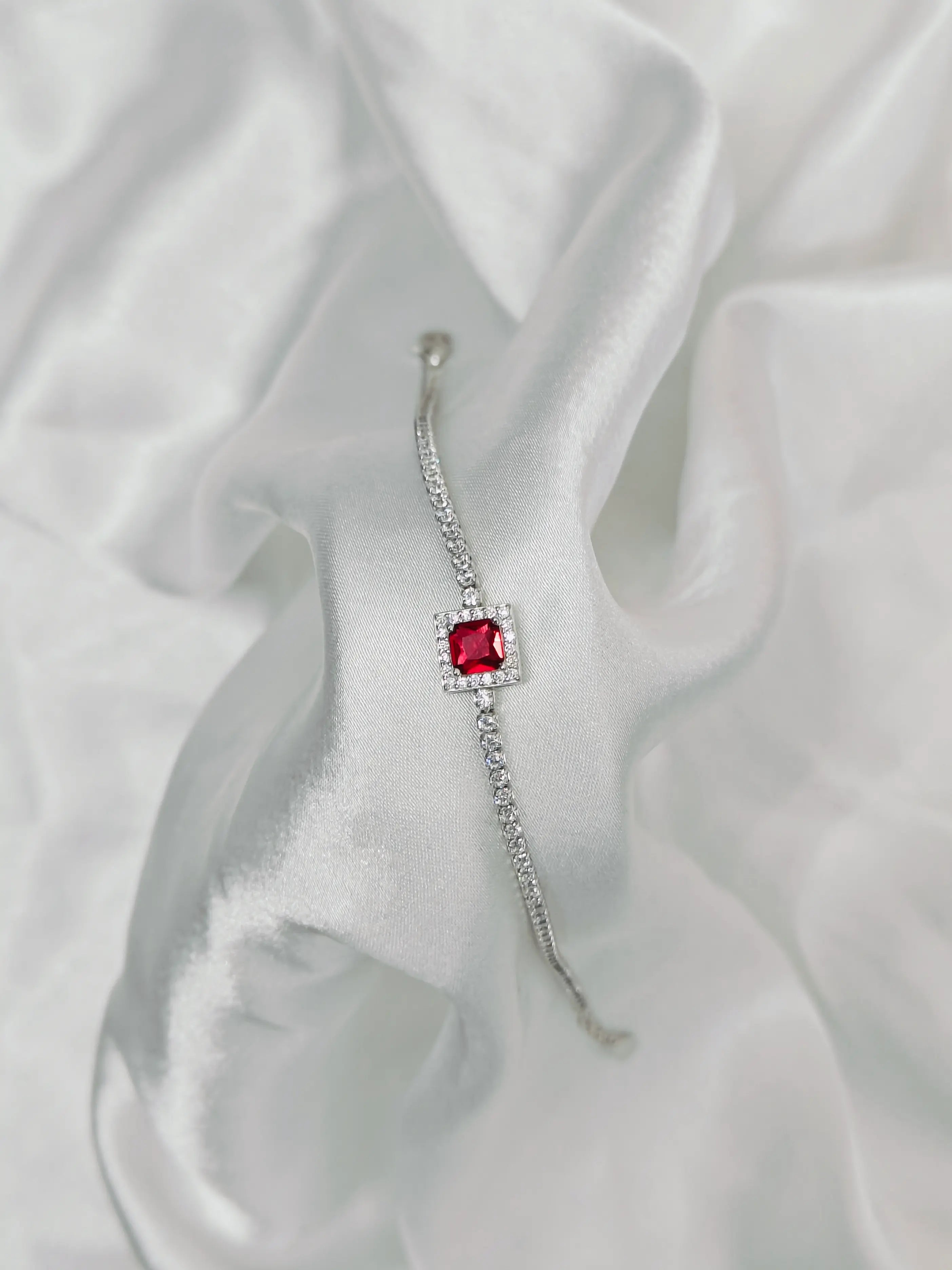 Silver earring with a red gemstone on a white fabric background