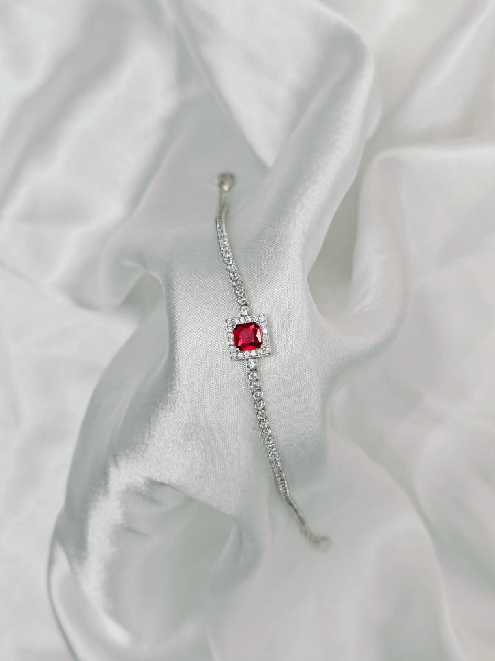 Silver earring with a red gemstone on a white fabric background