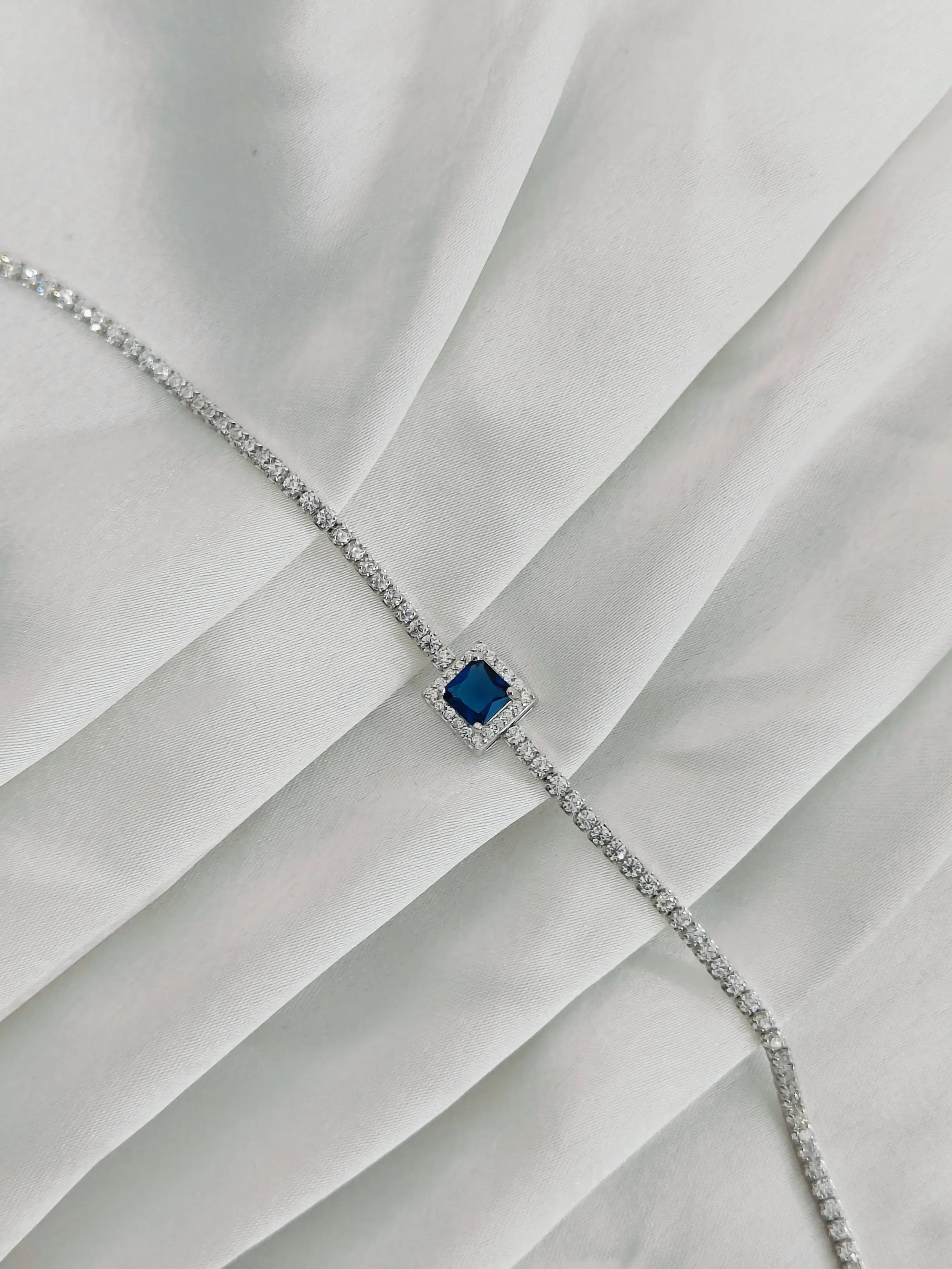 Silver bracelet with a blue gemstone on a white fabric background