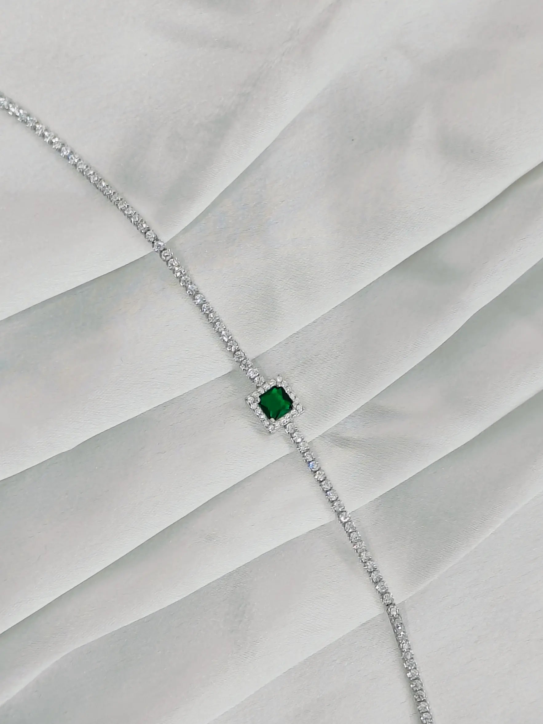 Diamond necklace with a central emerald stone on a white fabric background
