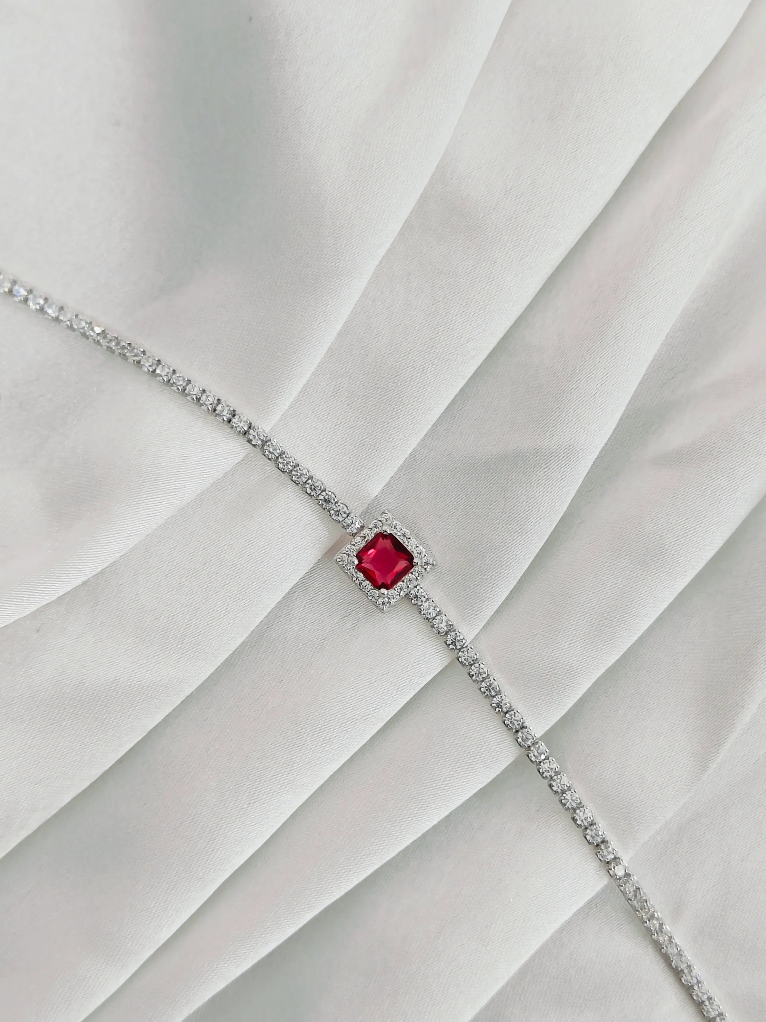 Silver bracelet with a red gemstone on a white fabric background