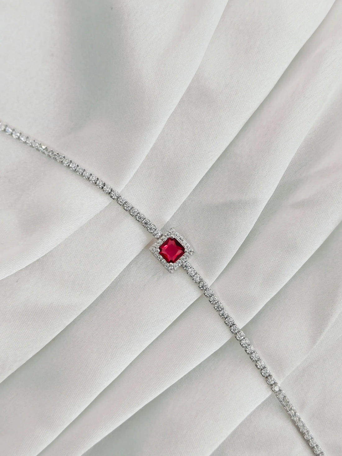 Silver bracelet with a red gemstone on a white fabric background