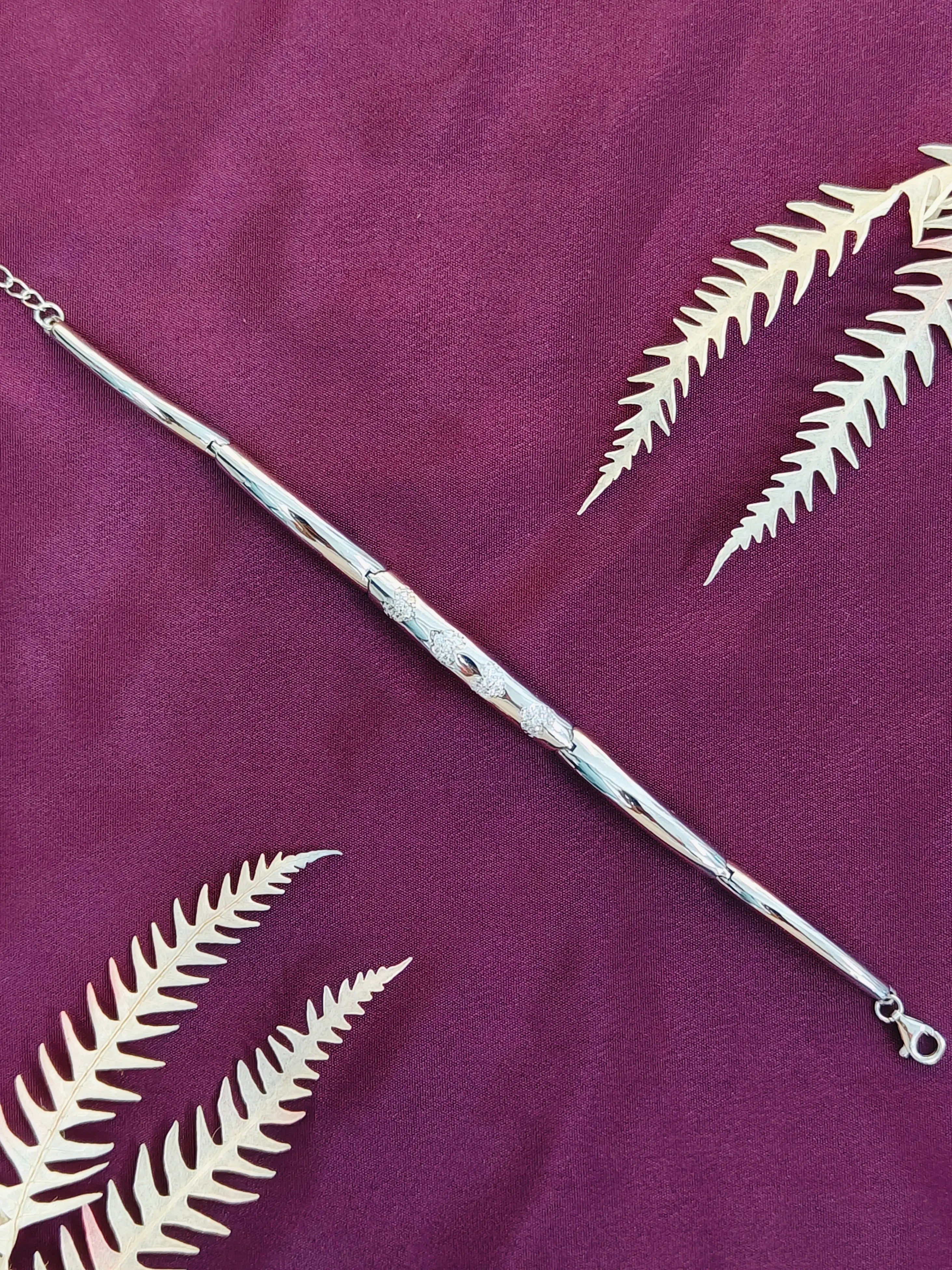 Silver bracelet with leaf designs on a purple fabric background