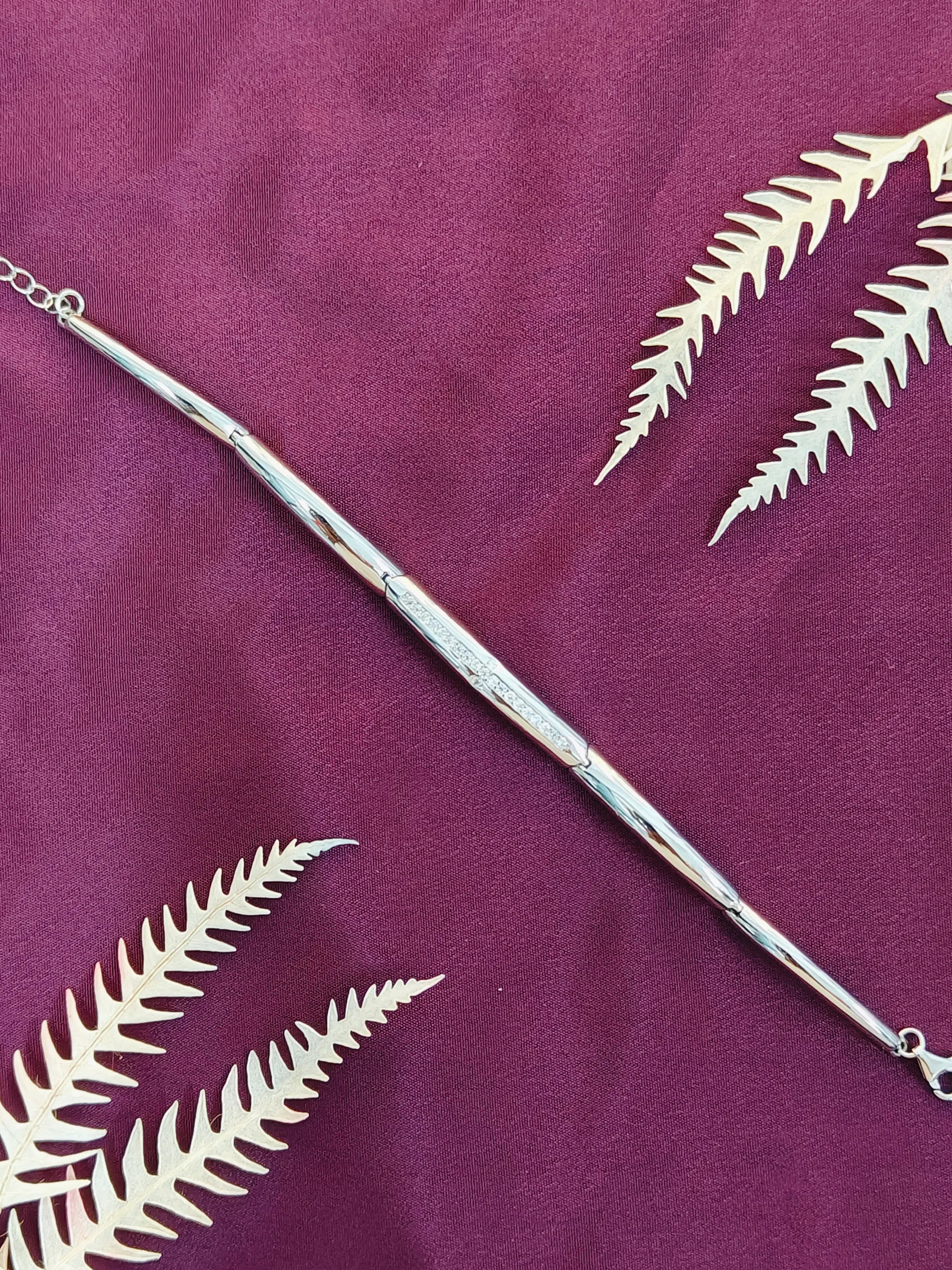 Silver bracelet with leaf designs on a purple fabric background