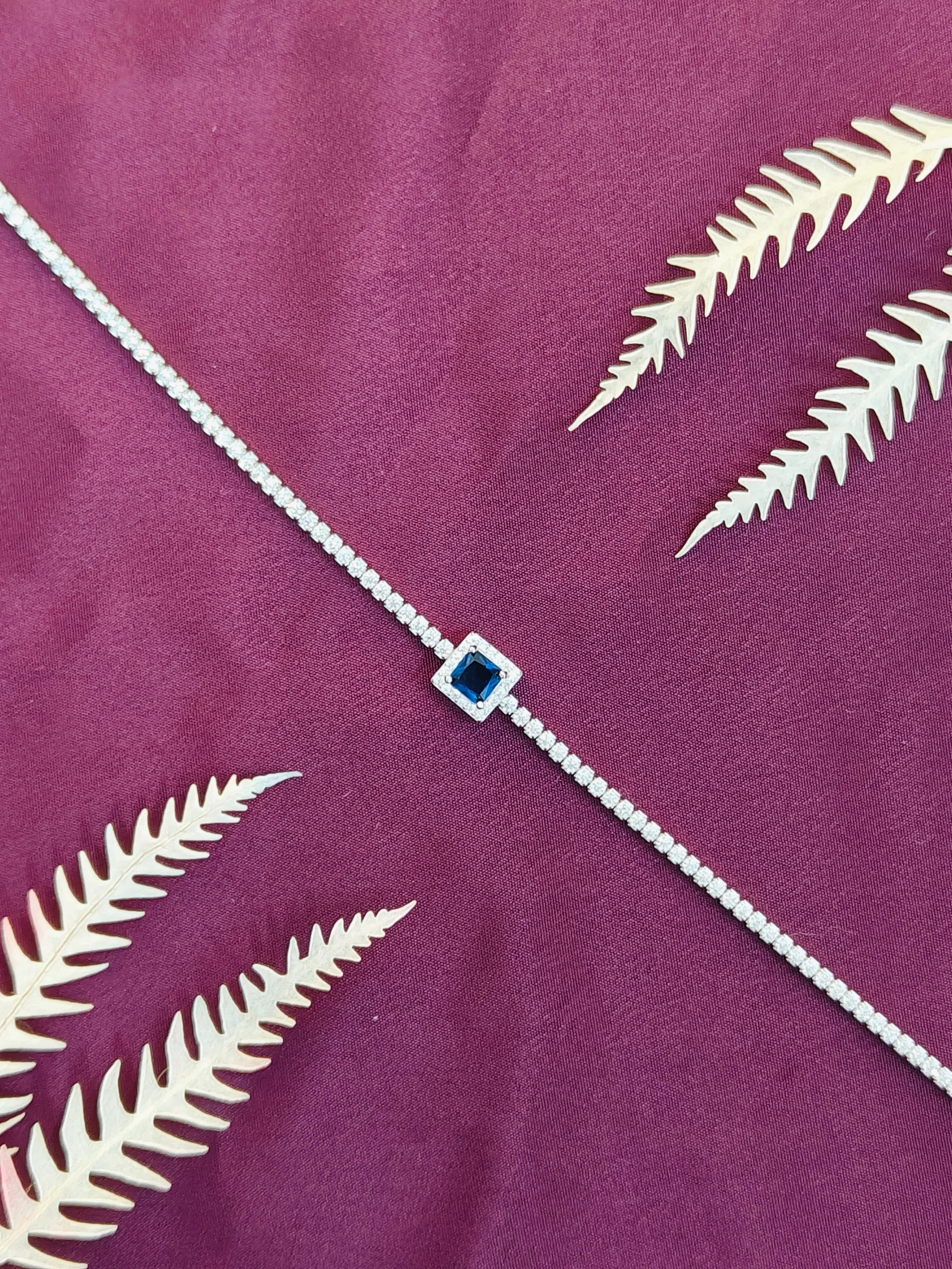 Silver bracelet with a blue gemstone on a purple fabric background with white leaf patterns
