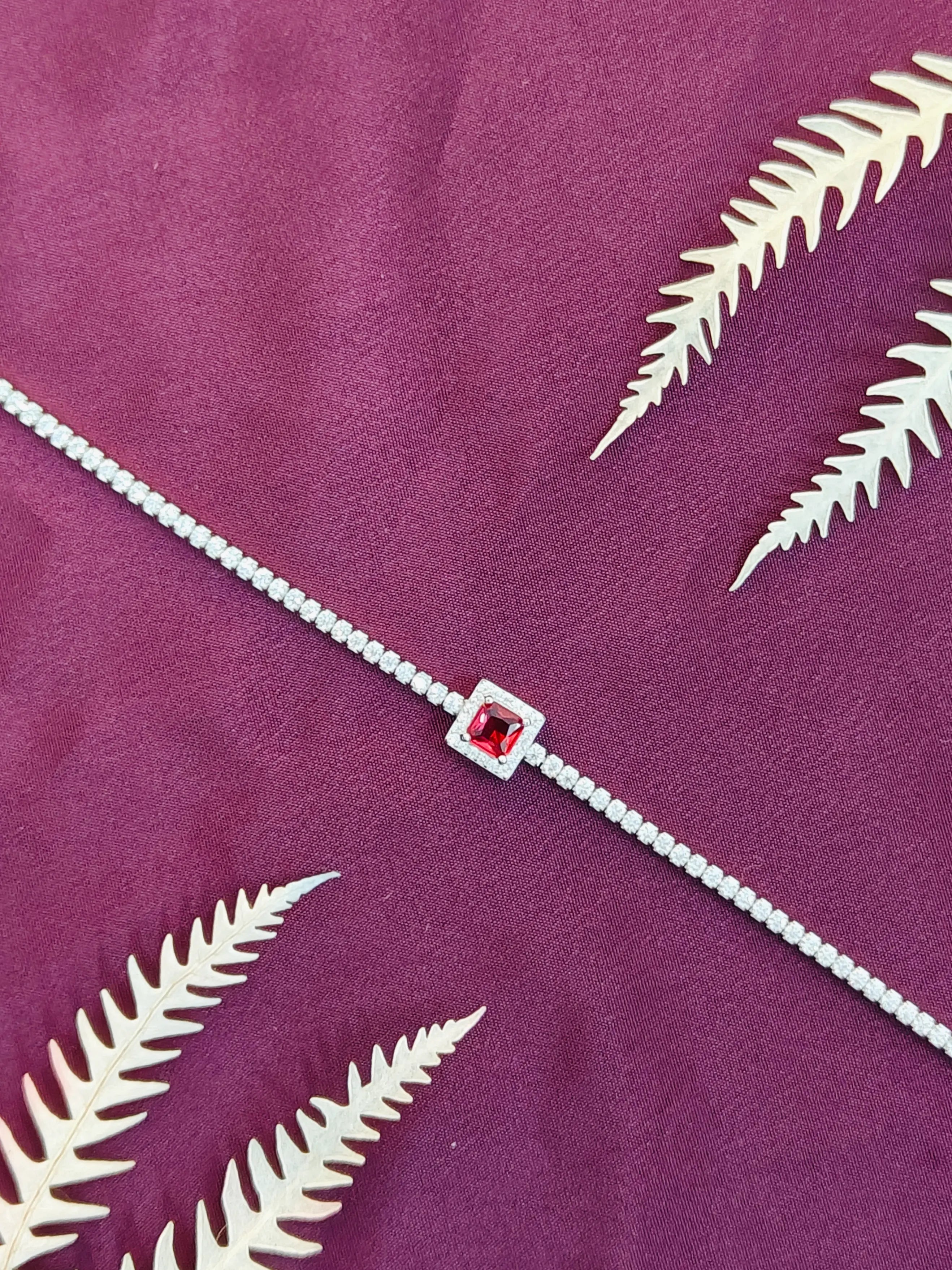 Silver bracelet with a red gemstone on a purple background with white leaf patterns