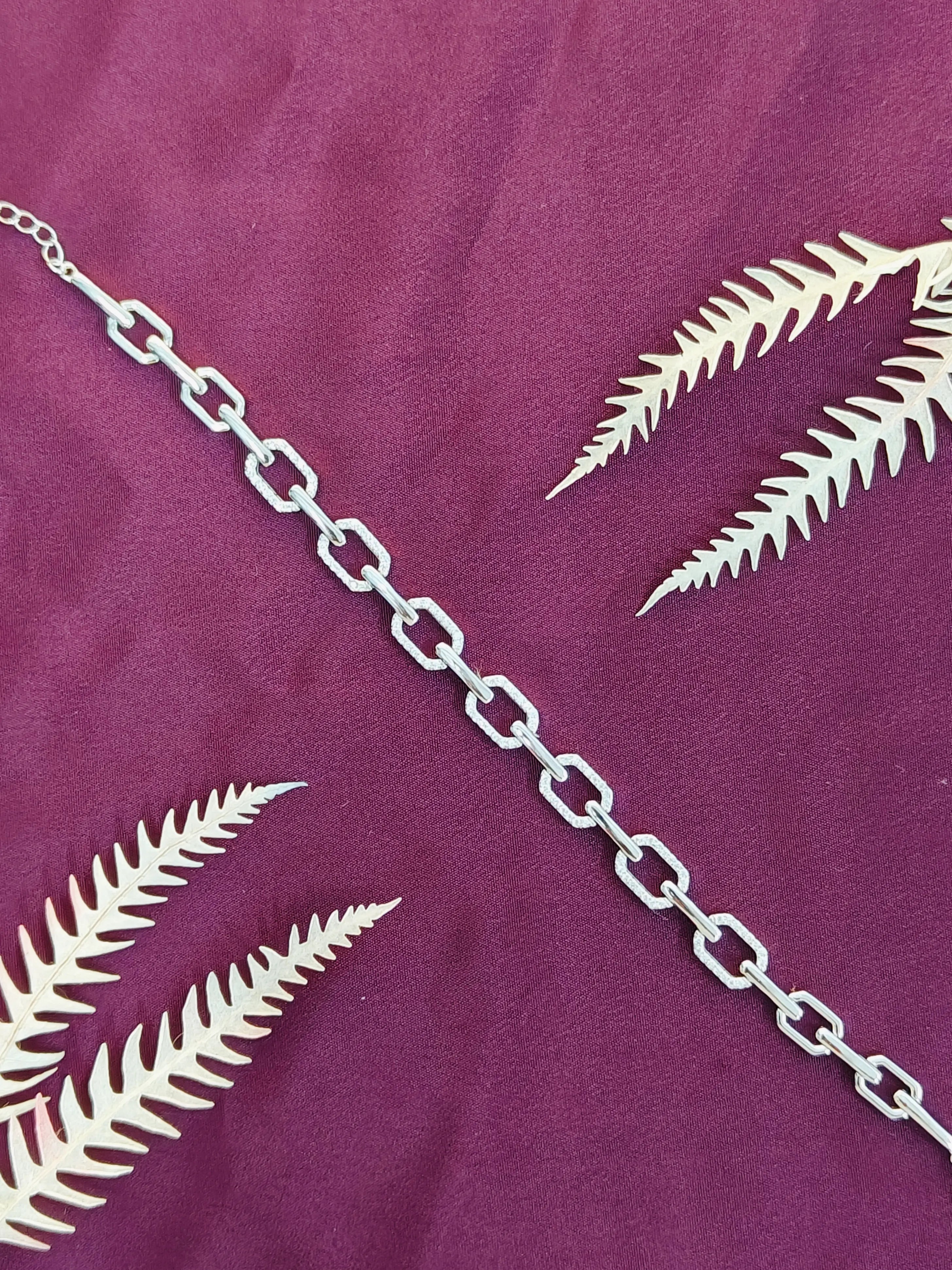 Silver chain and white fern leaves on a purple fabric background
