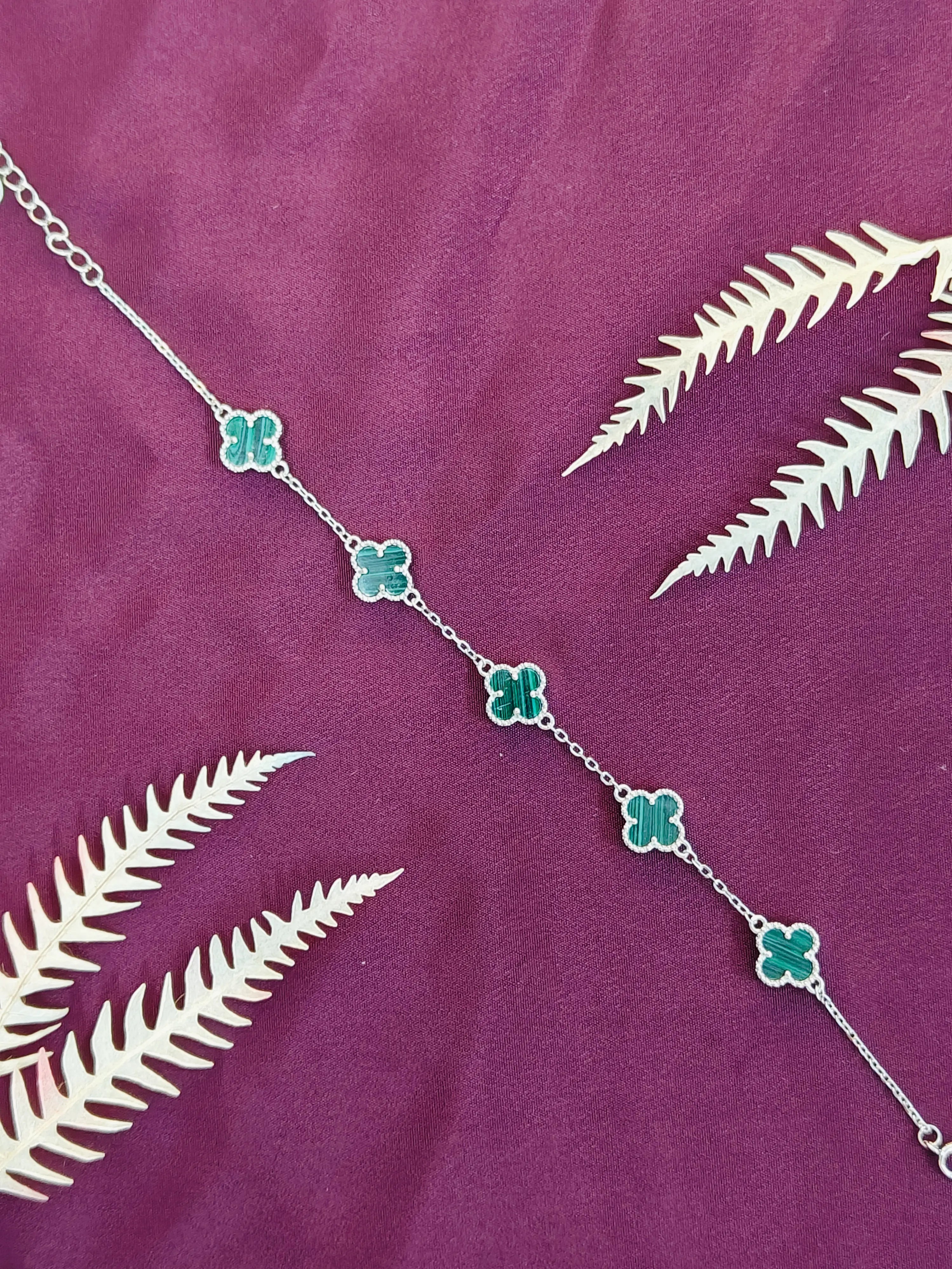 Silver necklace with green floral pendants on a purple fabric background