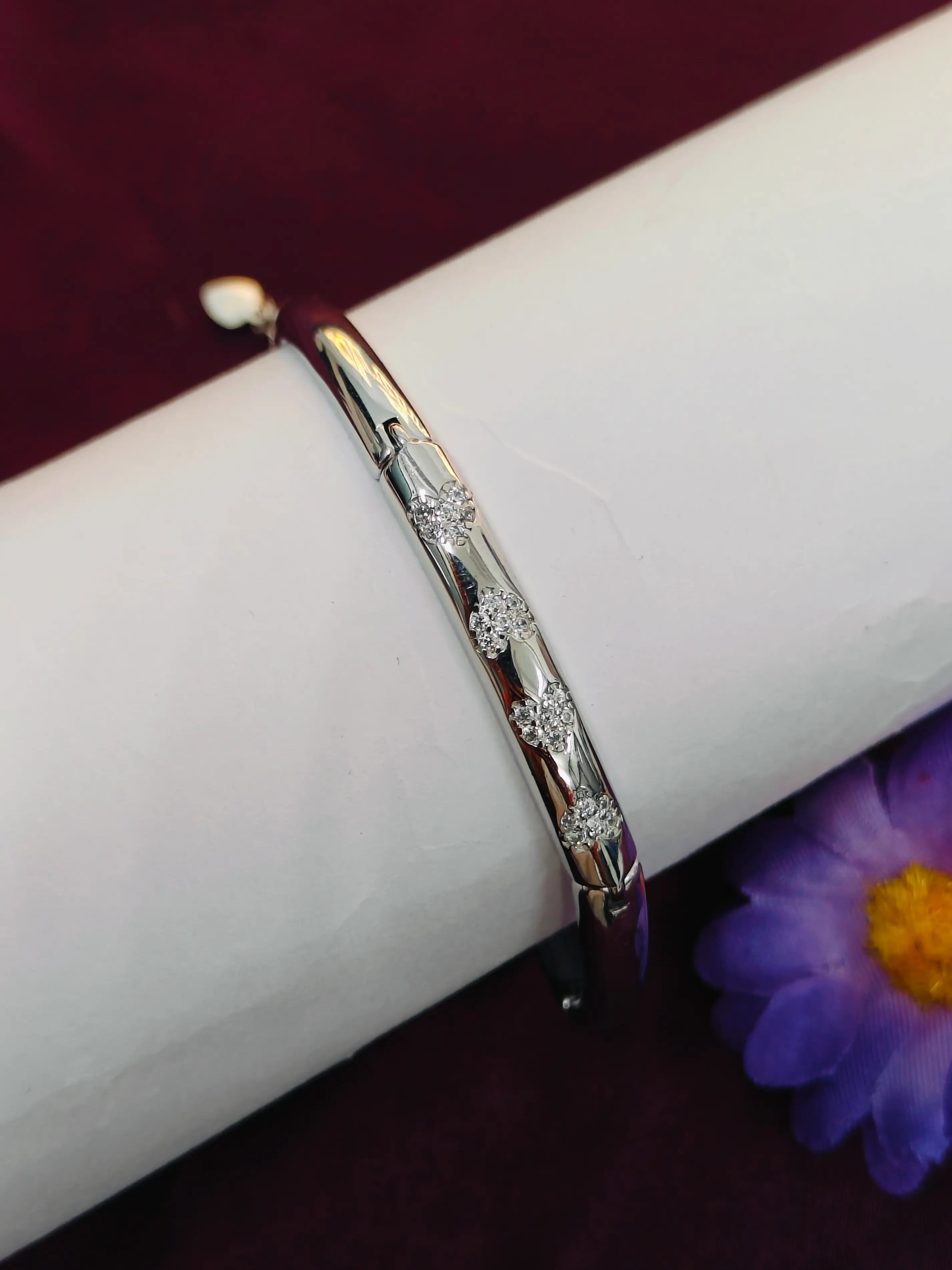 Silver bracelet with floral patterns on a white surface with a purple flower in the background