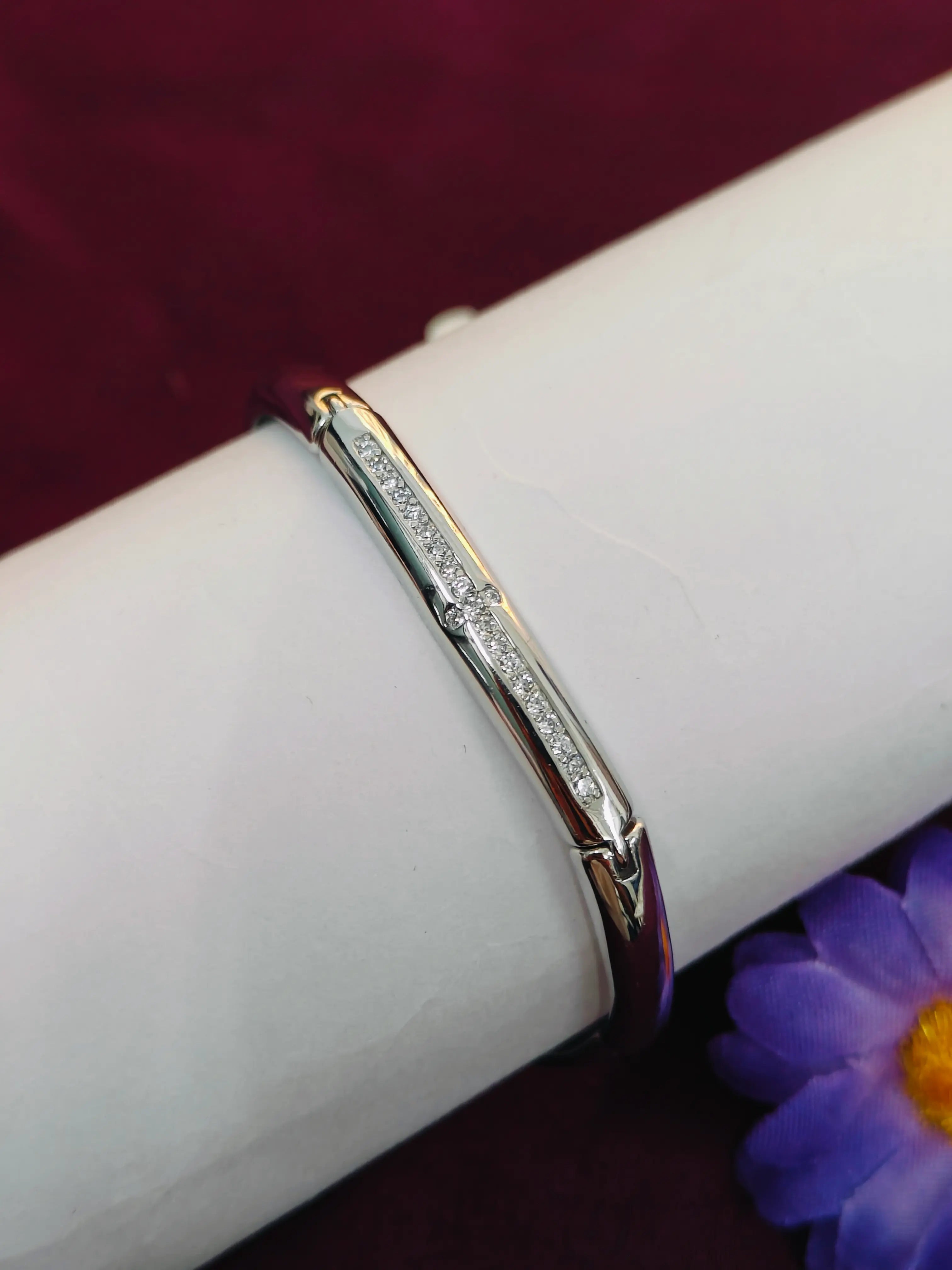 Silver bracelet with small diamonds on a white arm against a purple background