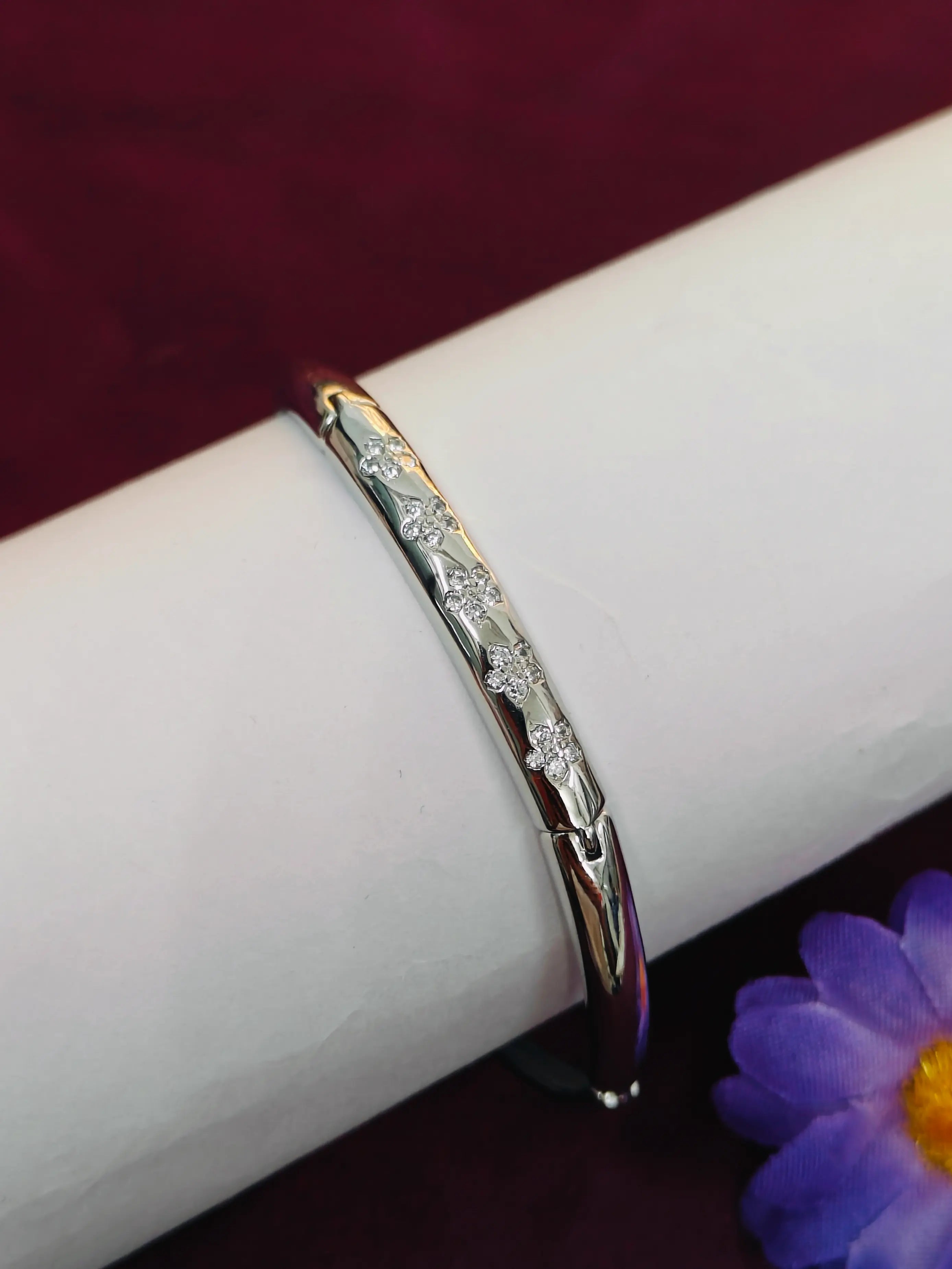 Gold bracelet with diamonds on a white surface with a purple flower in the corner