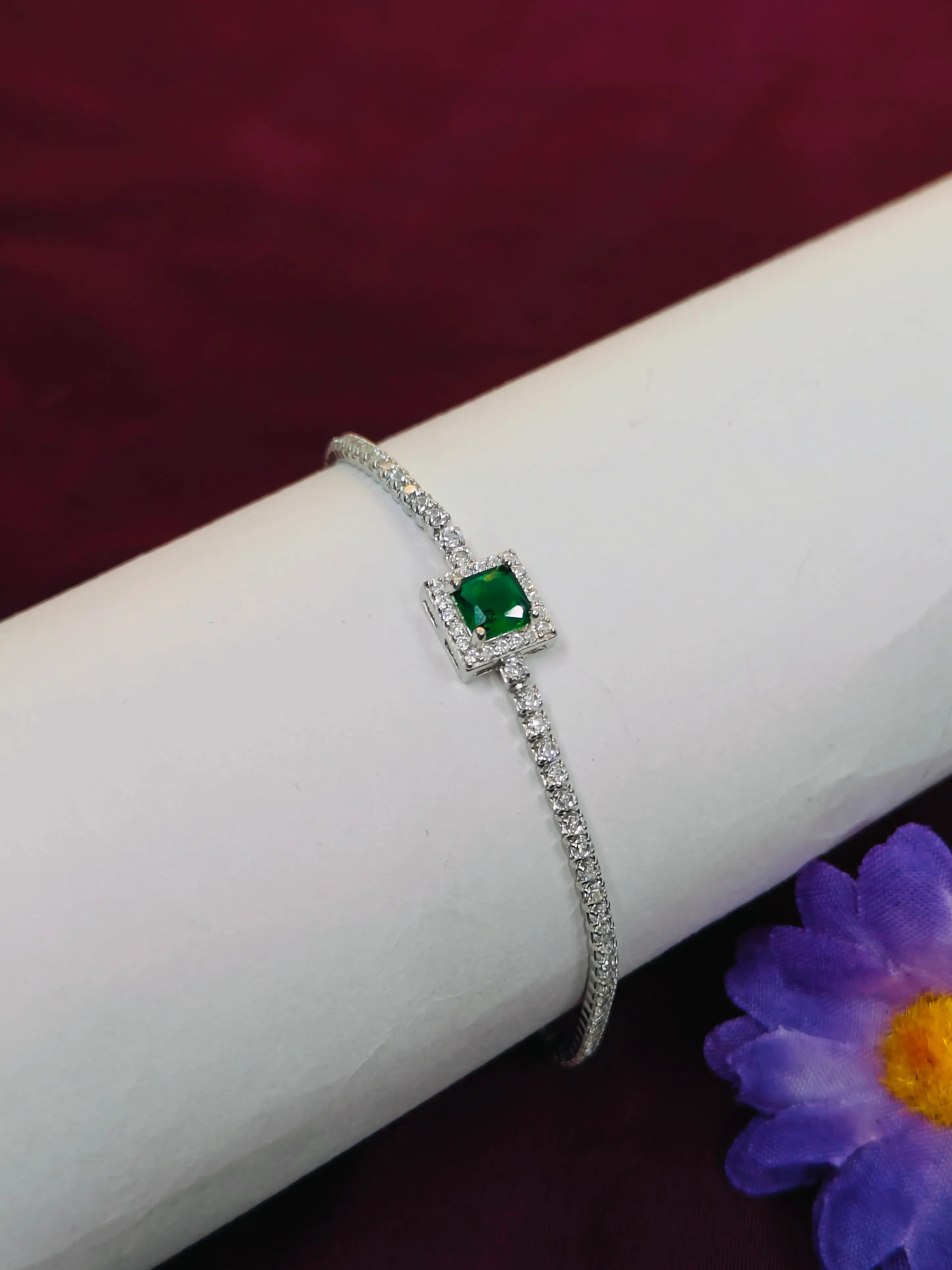 Silver bracelet with a green gemstone on a white arm with a purple flower in the background