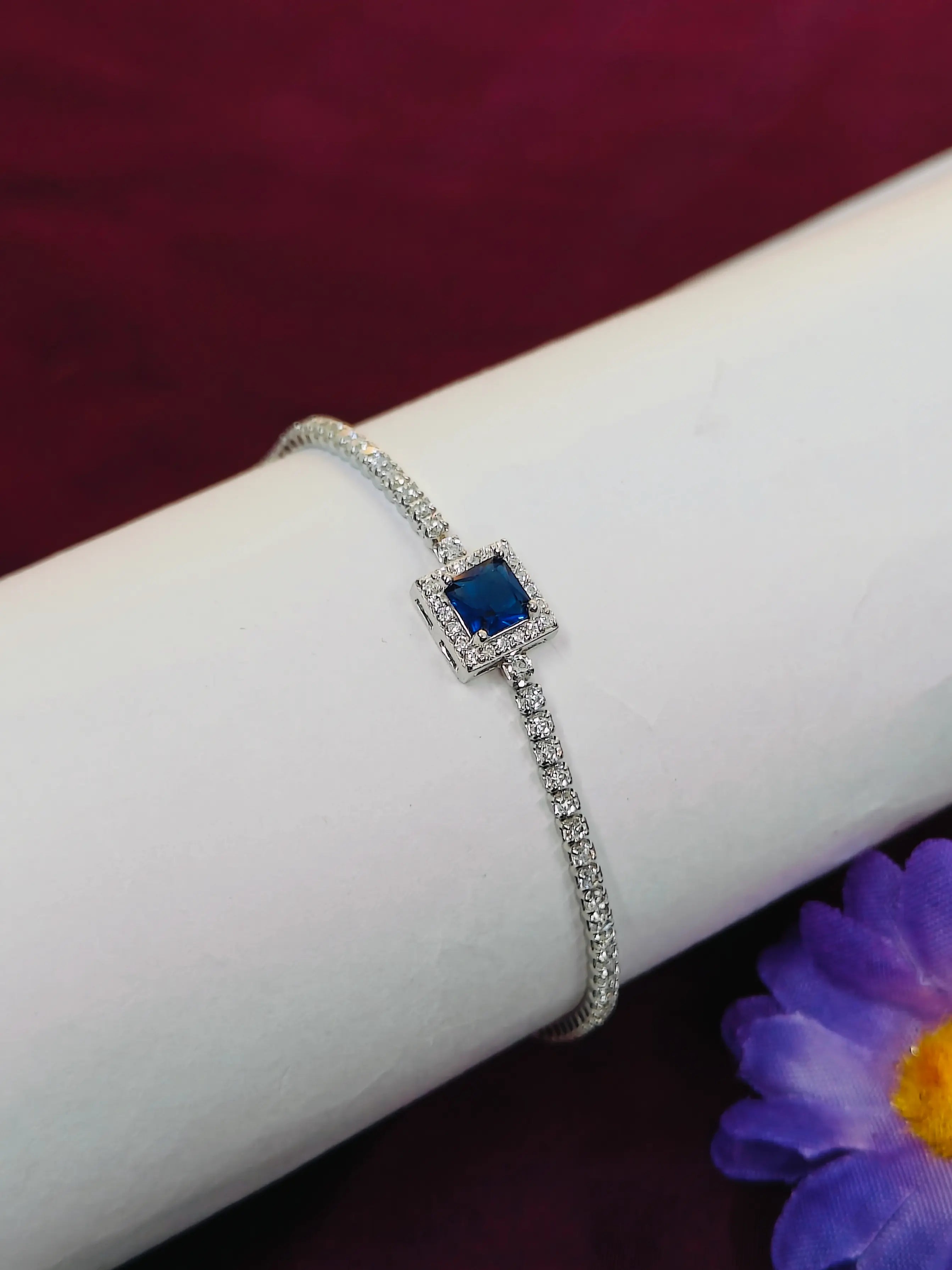 Silver bracelet with a blue gemstone on a white arm against a purple background