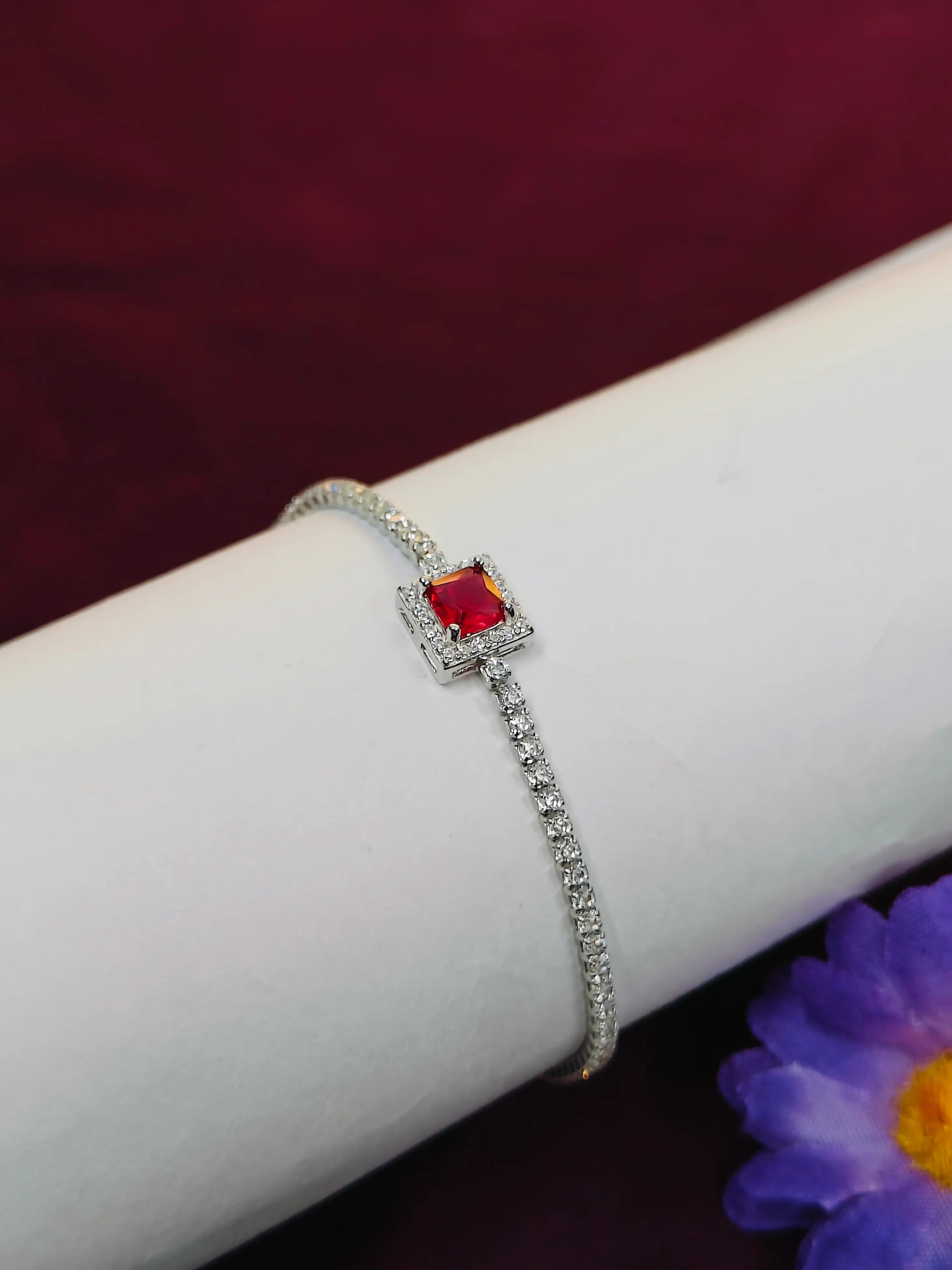 Silver bracelet with a red gemstone on a wrist against a dark background
