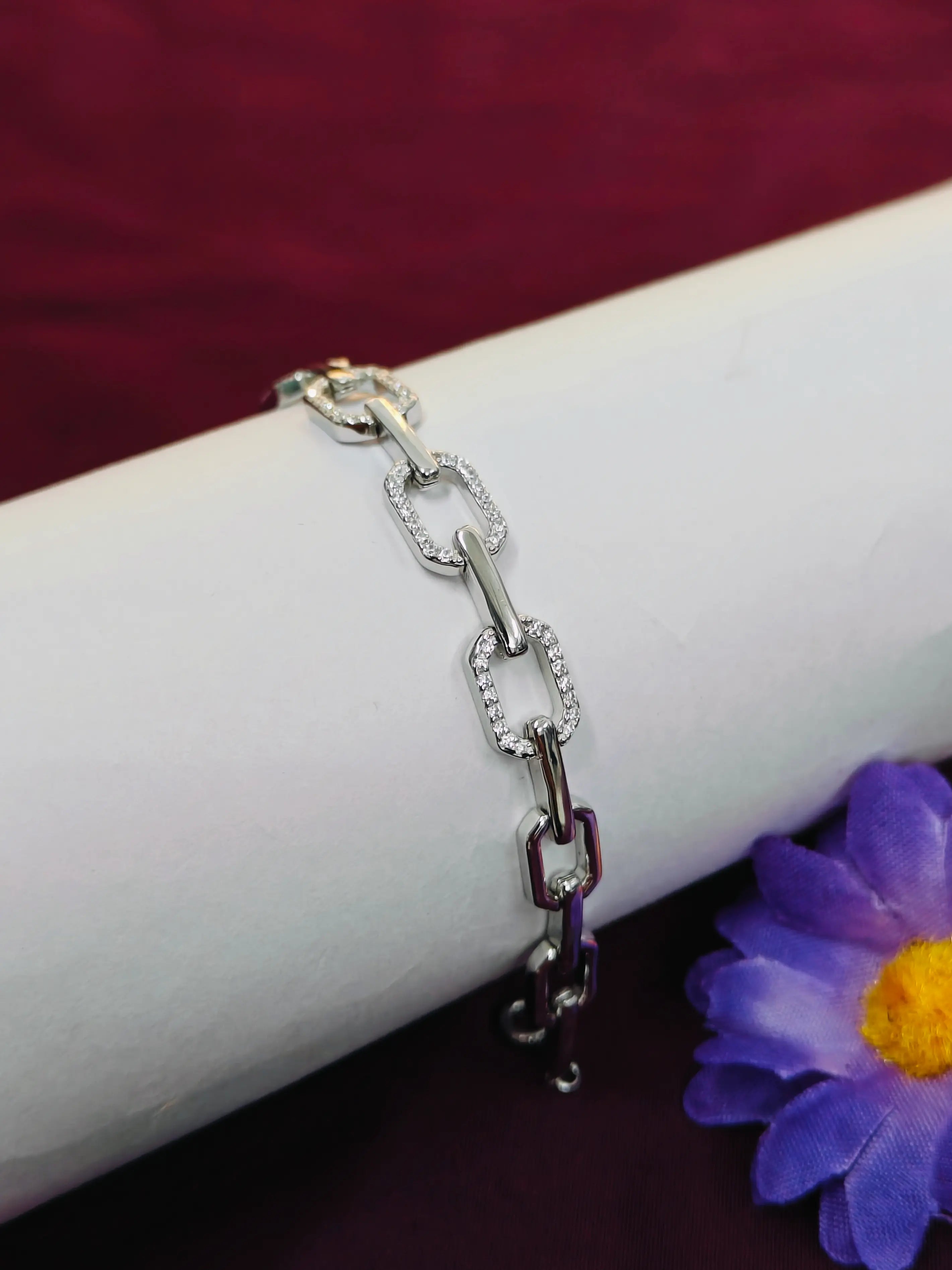 Silver chain bracelet on a white surface with a purple flower in the background