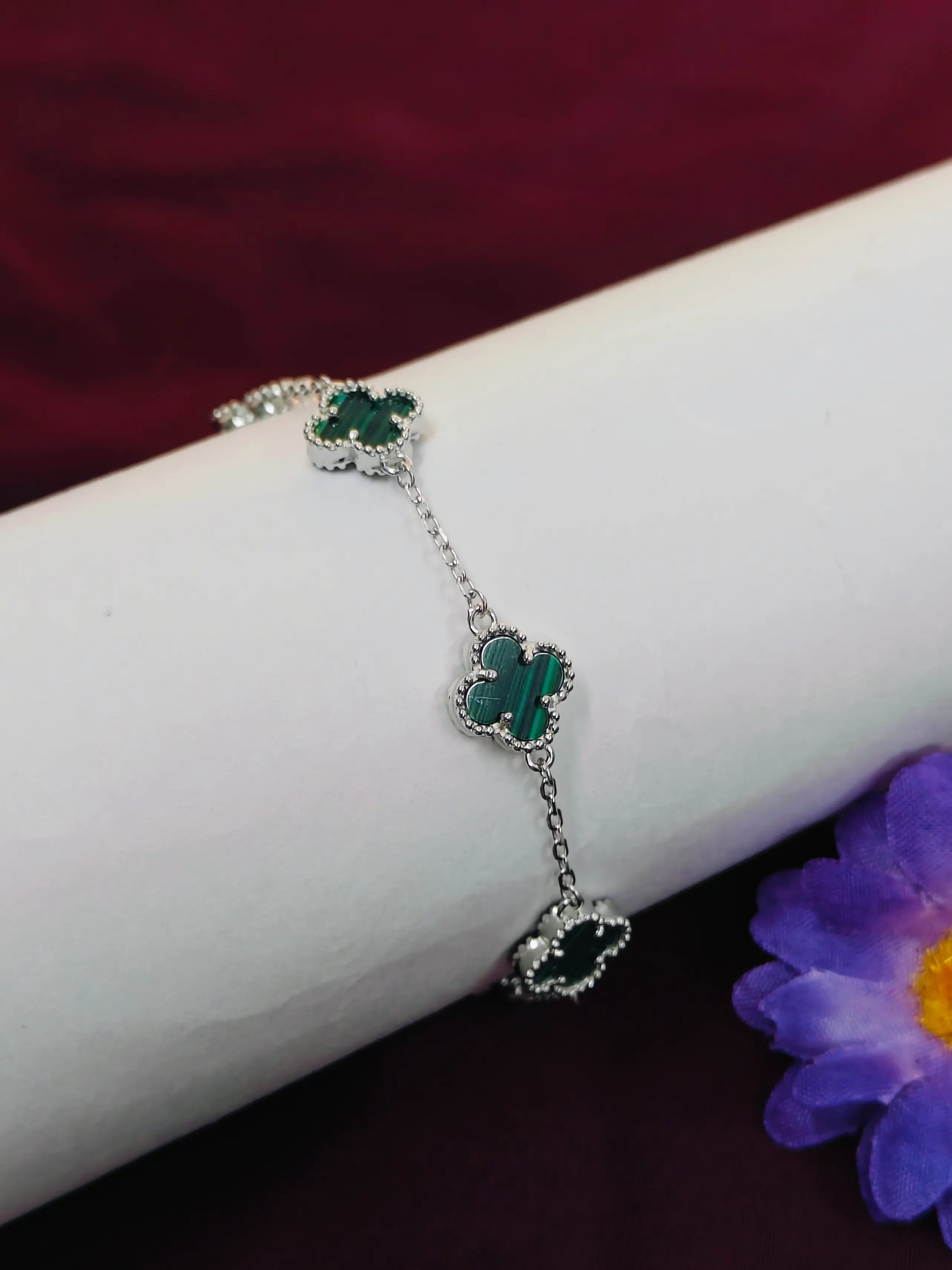 Silver bracelet with green stones on a wrist against a dark background
