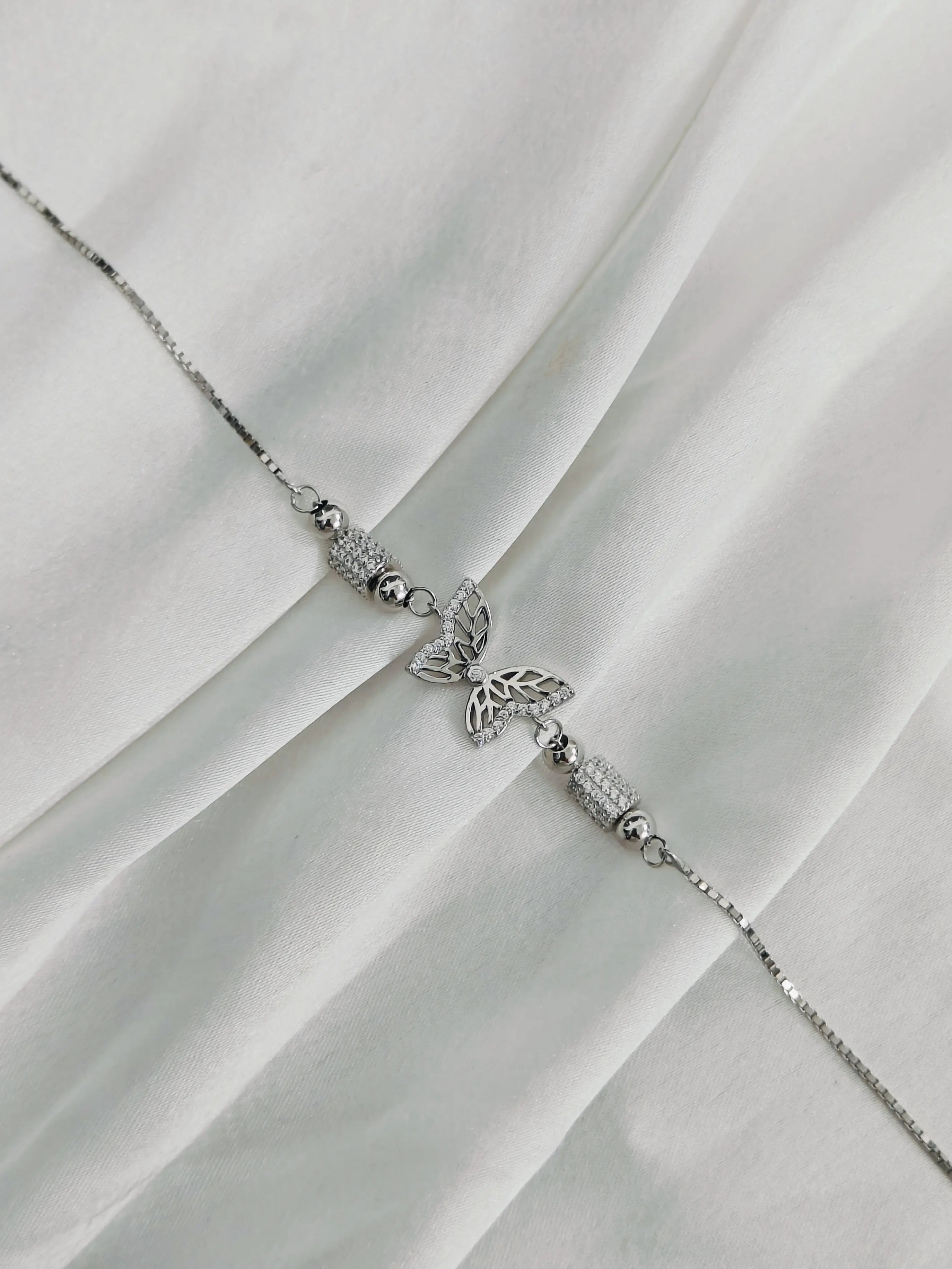 Silver bracelet with butterfly charm on a white fabric background