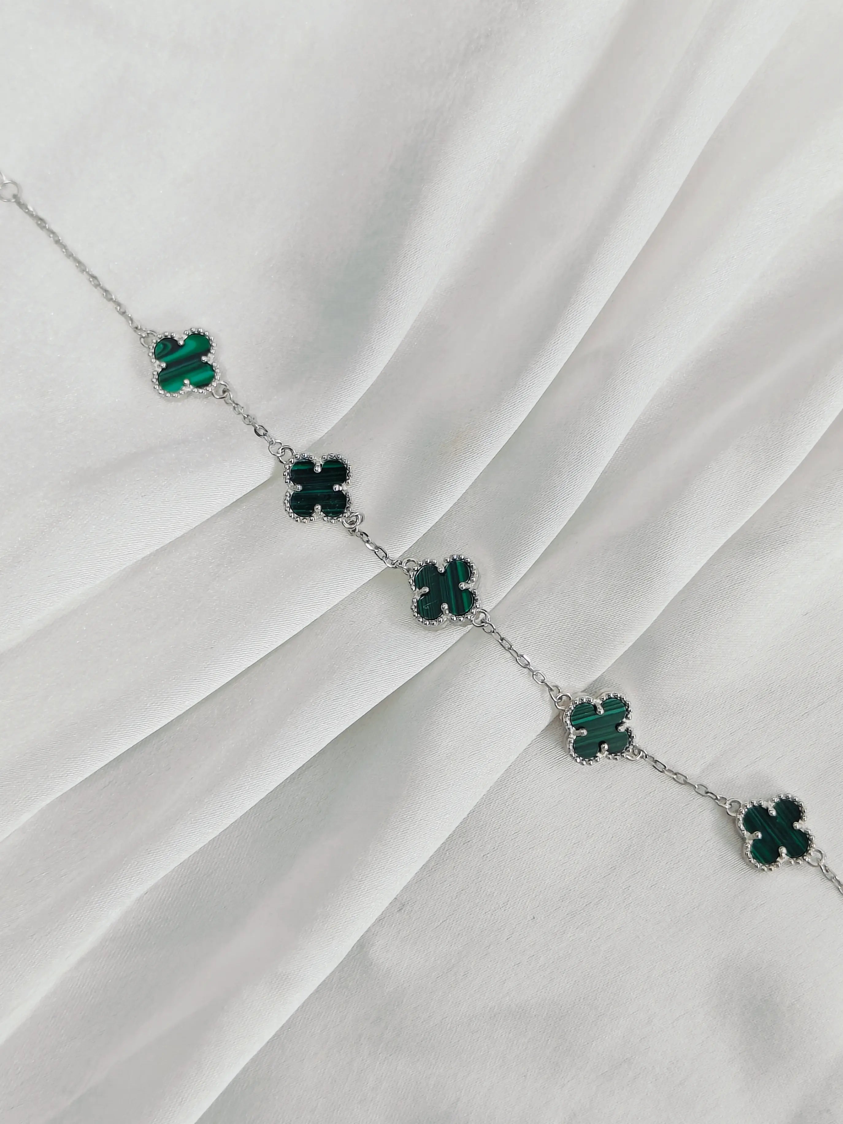 Silver necklace with green clover-shaped pendants on a white fabric background