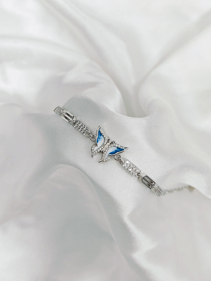 Silver bracelet with a butterfly charm on a white fabric background