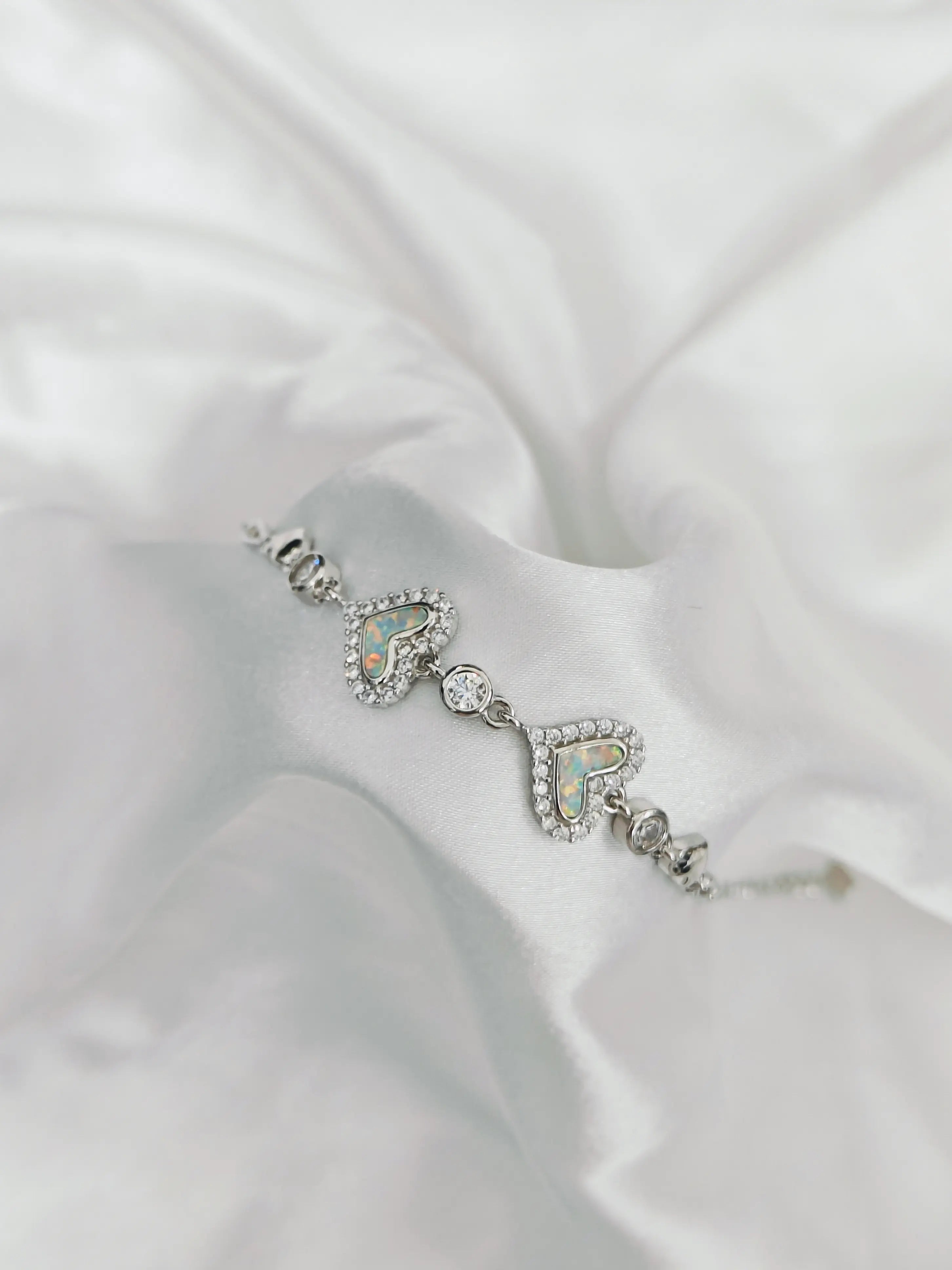 Silver bracelet with heart and 'R' design on a white fabric background