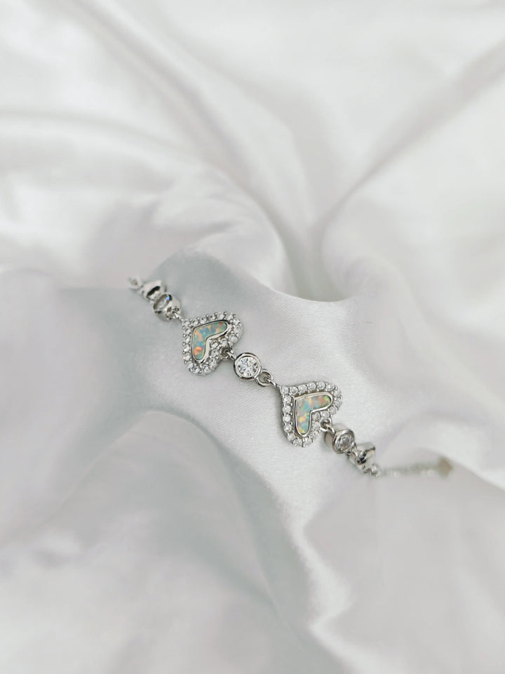 Silver bracelet with heart and 'R' design on a white fabric background