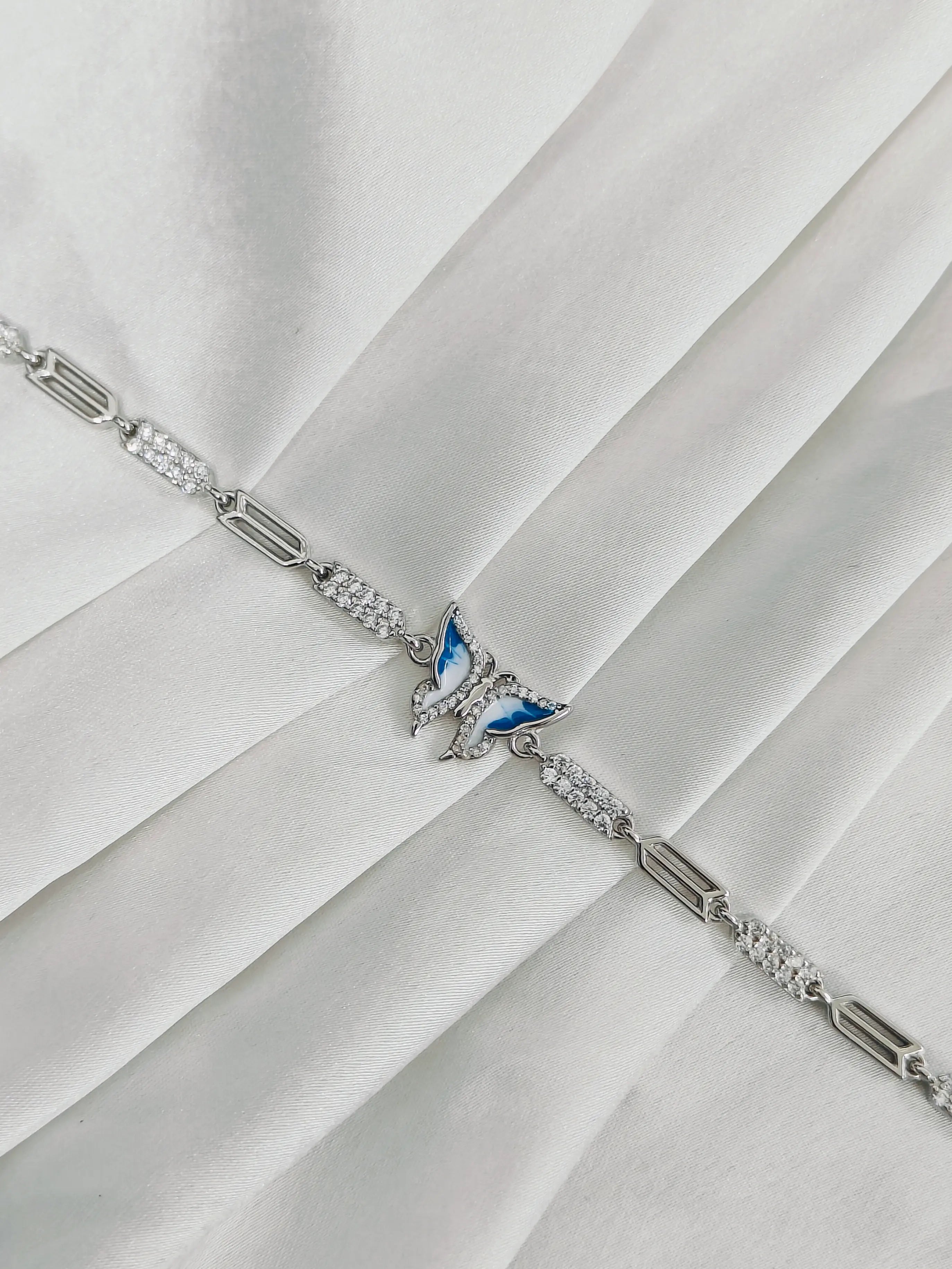 Silver bracelet with a butterfly charm on a white fabric background
