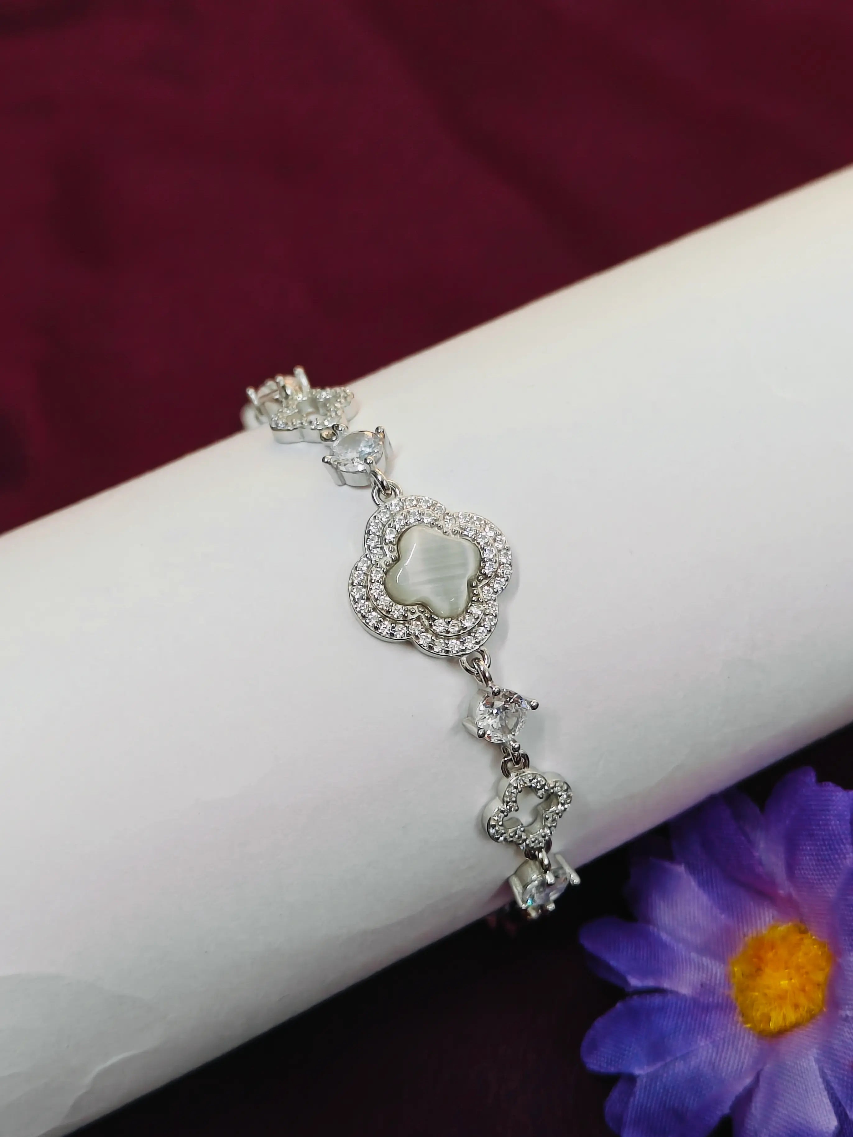 Silver bracelet with a heart-shaped center on a wrist, against a dark background with a purple flower.