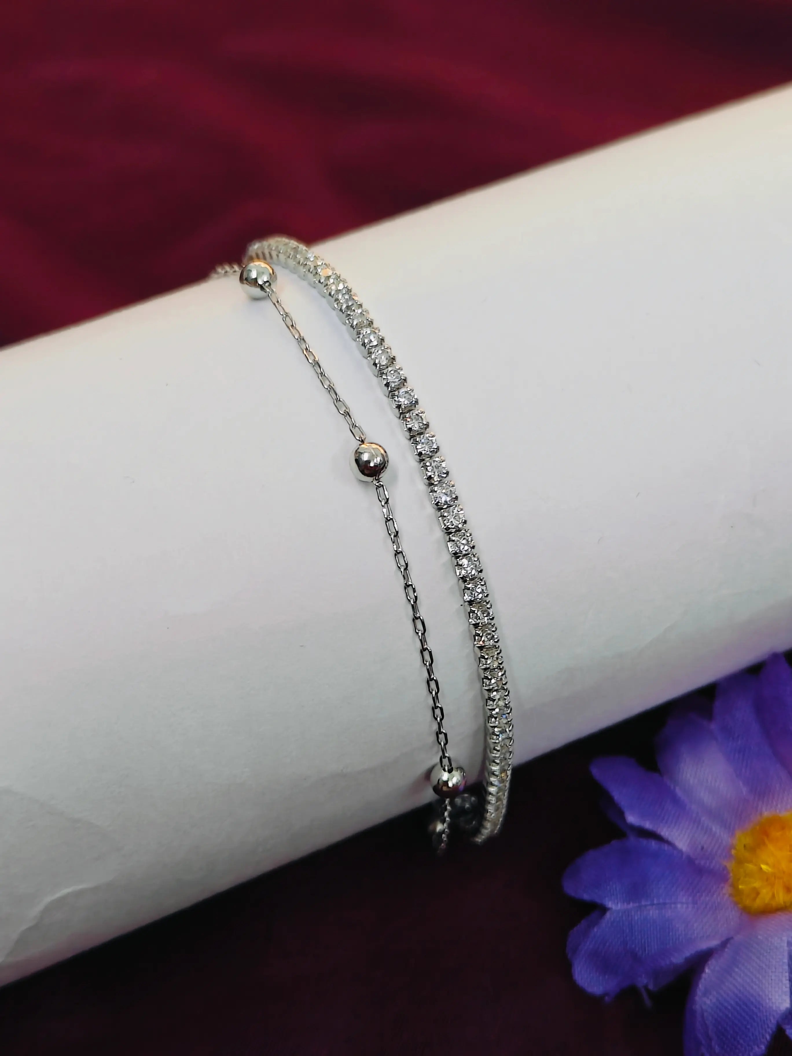 Two silver bracelets on a white surface with a purple flower in the background