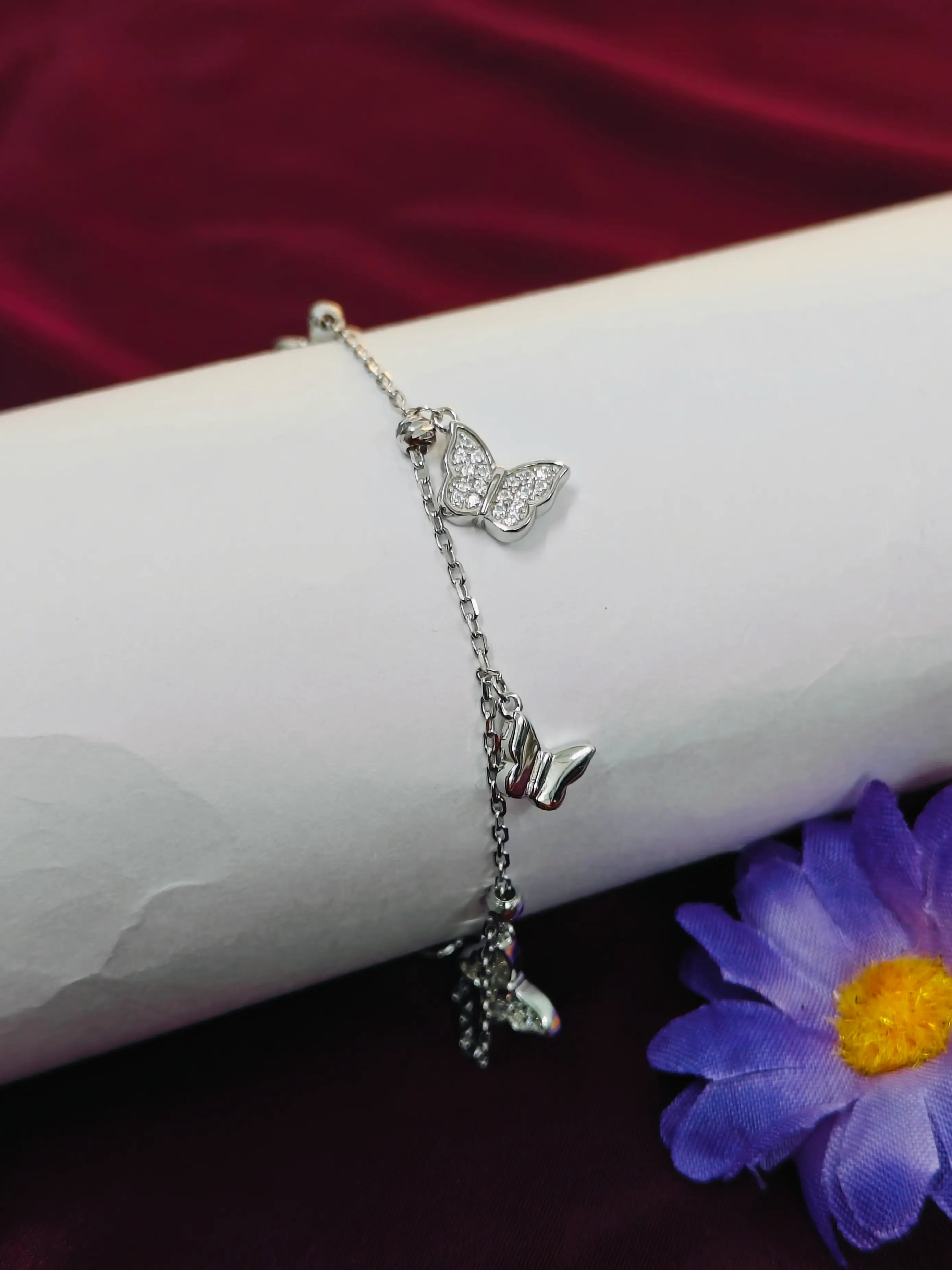 Silver bracelet with butterfly charms on a white arm against a red background with a purple flower.