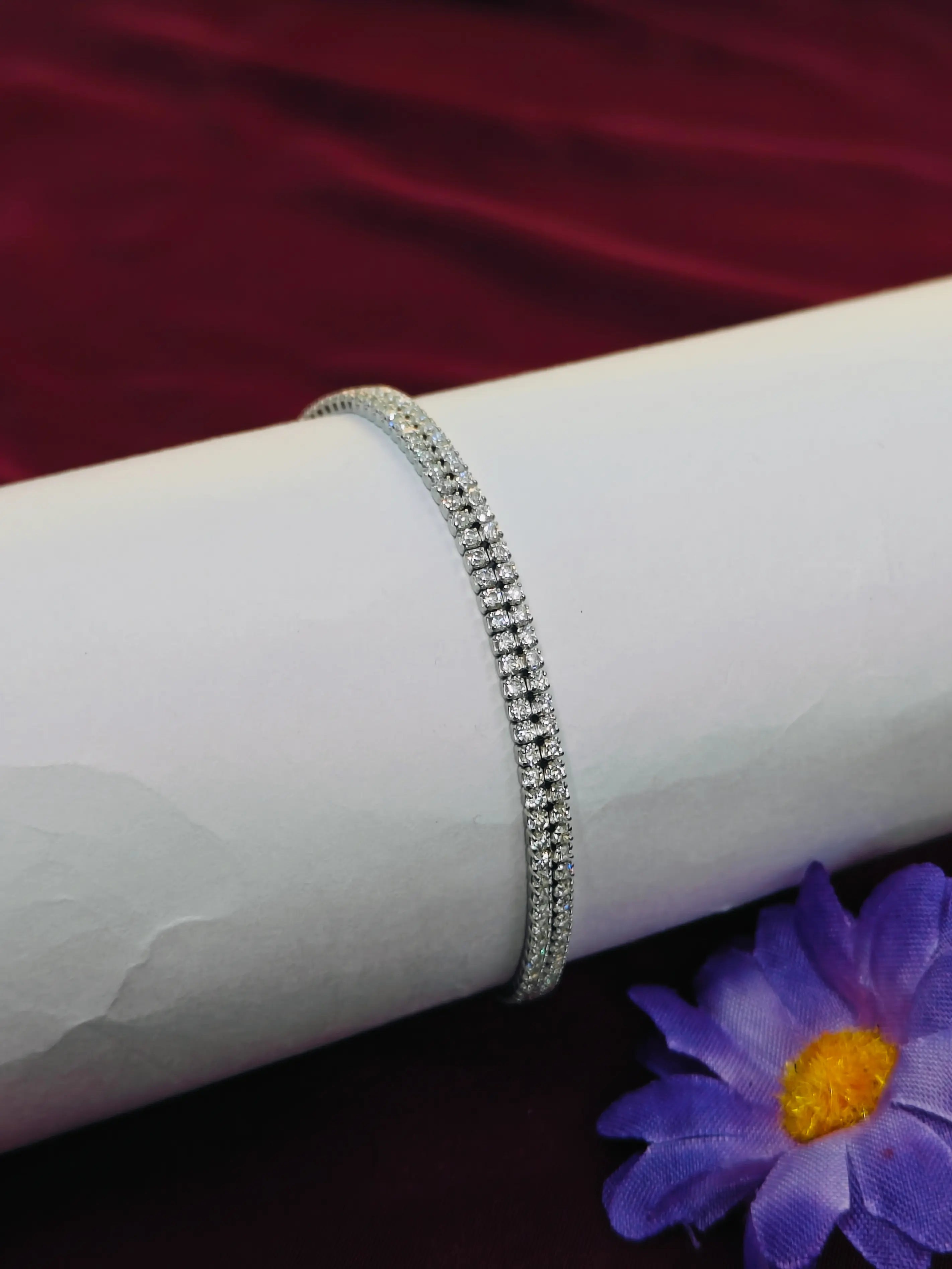 Silver bracelet on a white arm with a purple flower in the background