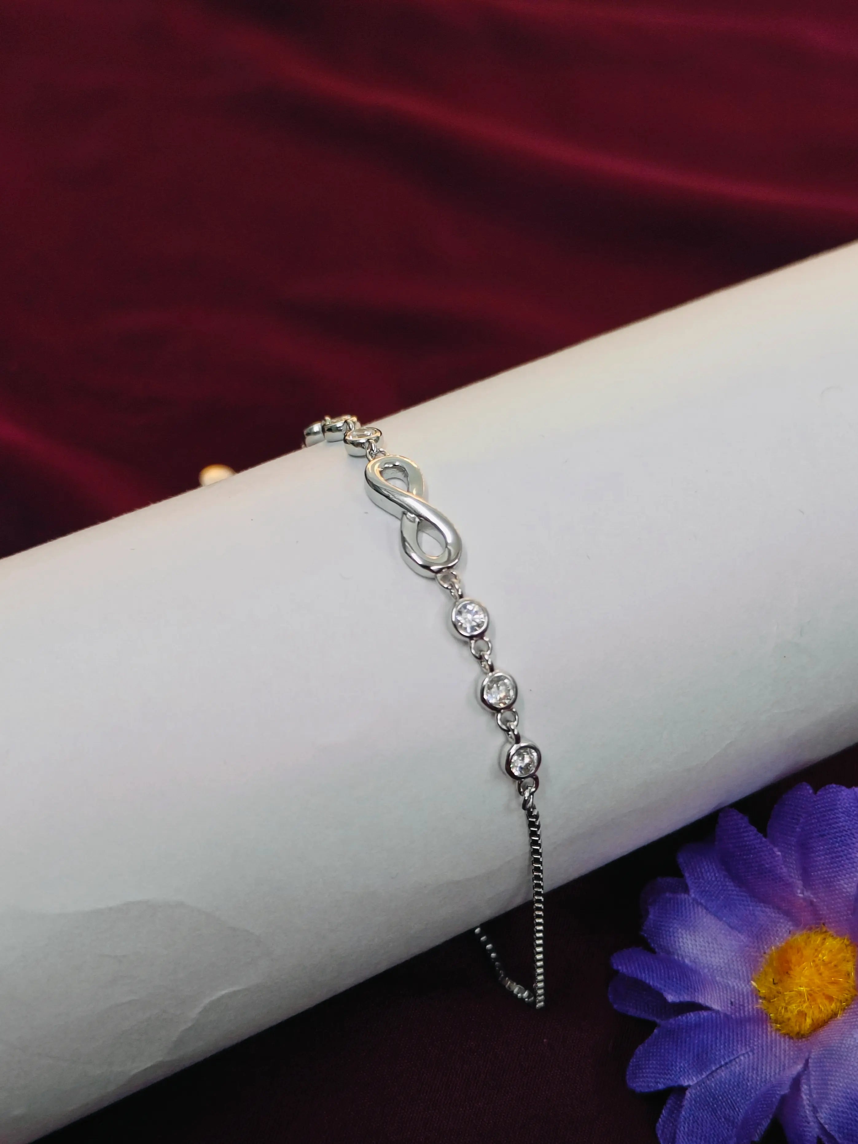 Silver bracelet with infinity symbol on a white arm against a red background