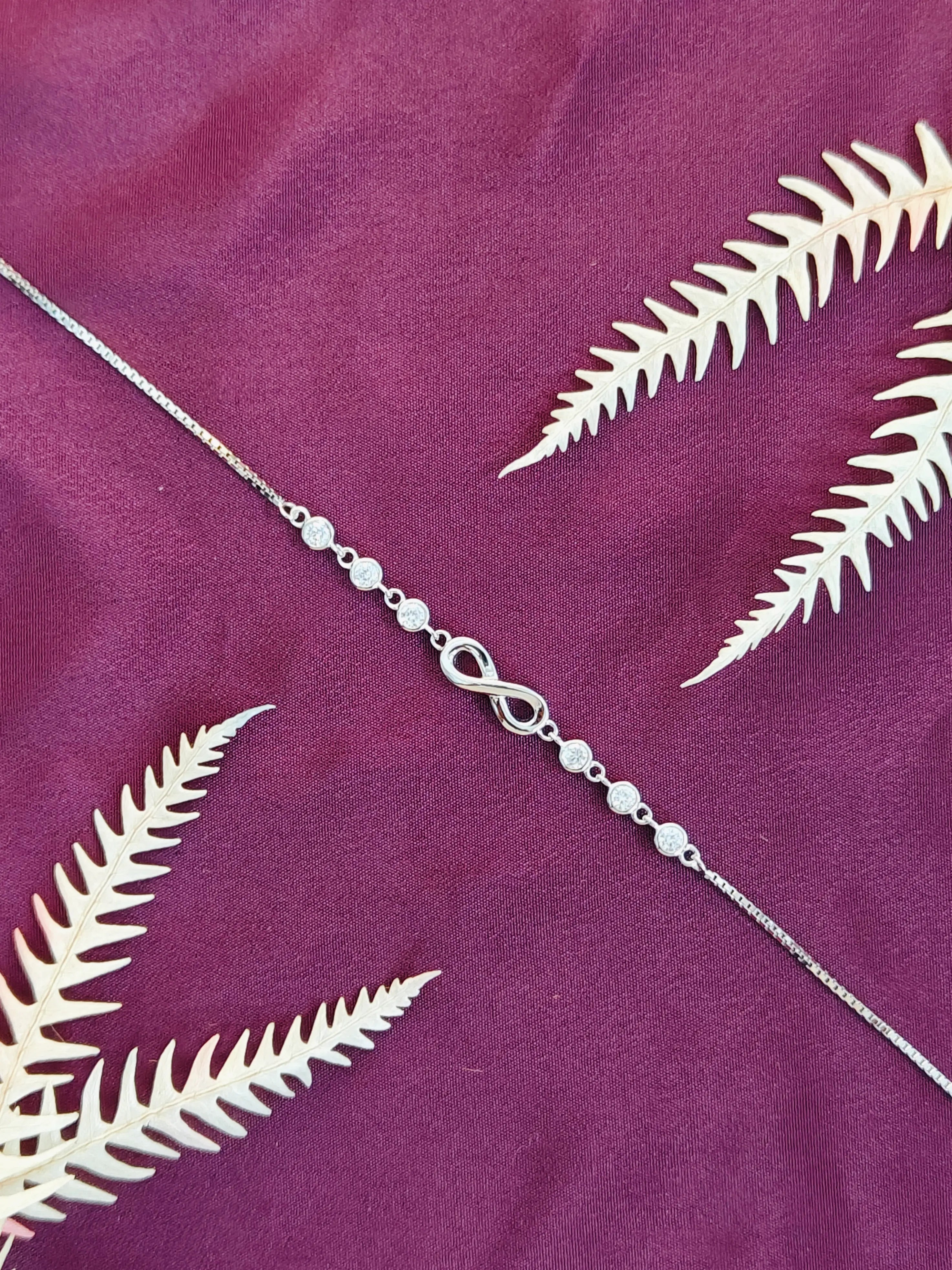 Silver anklet with beads on a purple fabric background with white leaf patterns
