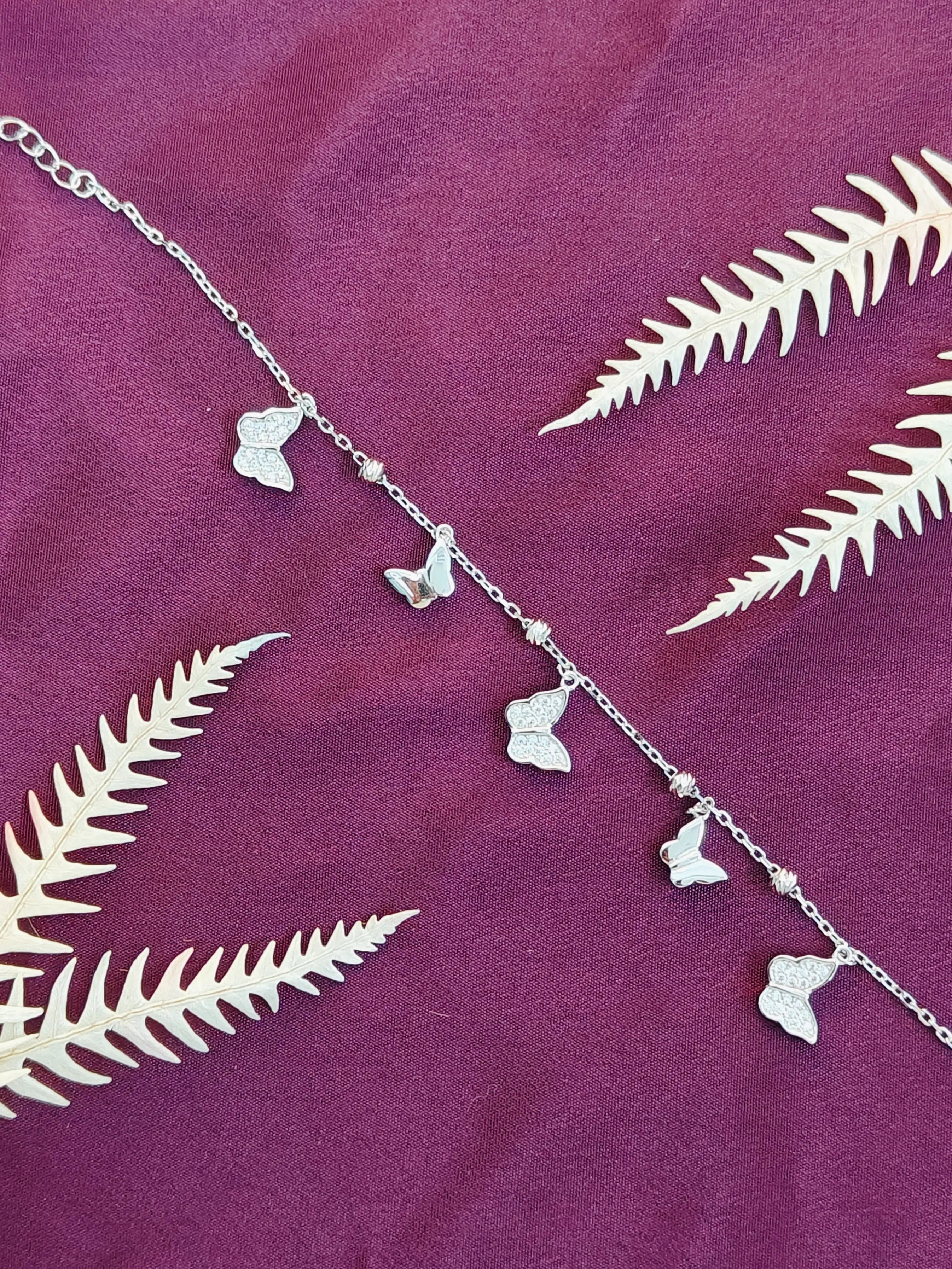Silver anklets with leaf-shaped charms on a purple fabric background