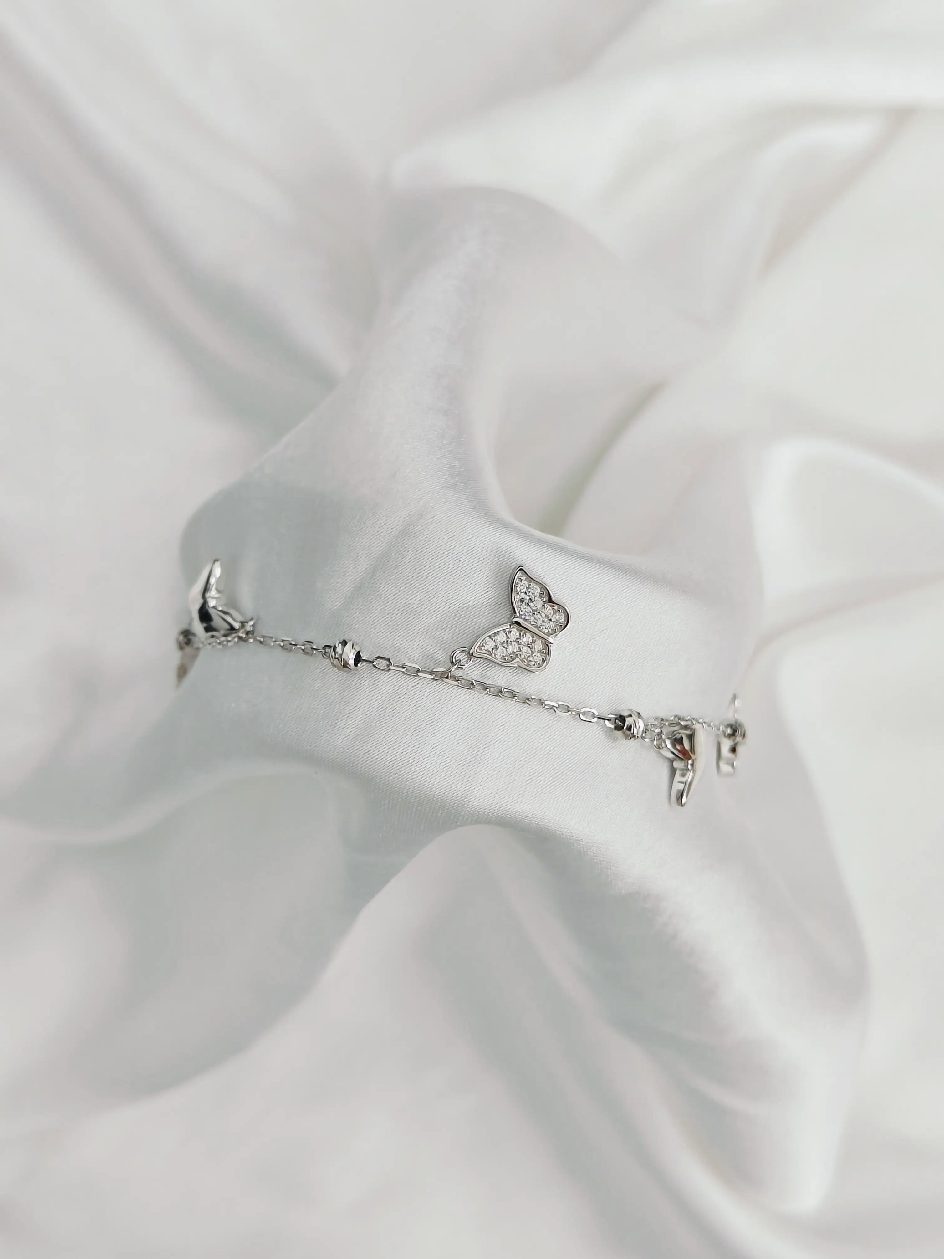 Silver bracelet with butterfly charm on a white satin background