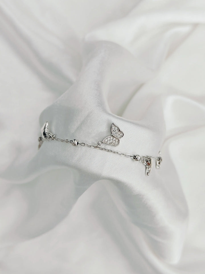 Silver bracelet with butterfly charm on a white satin background