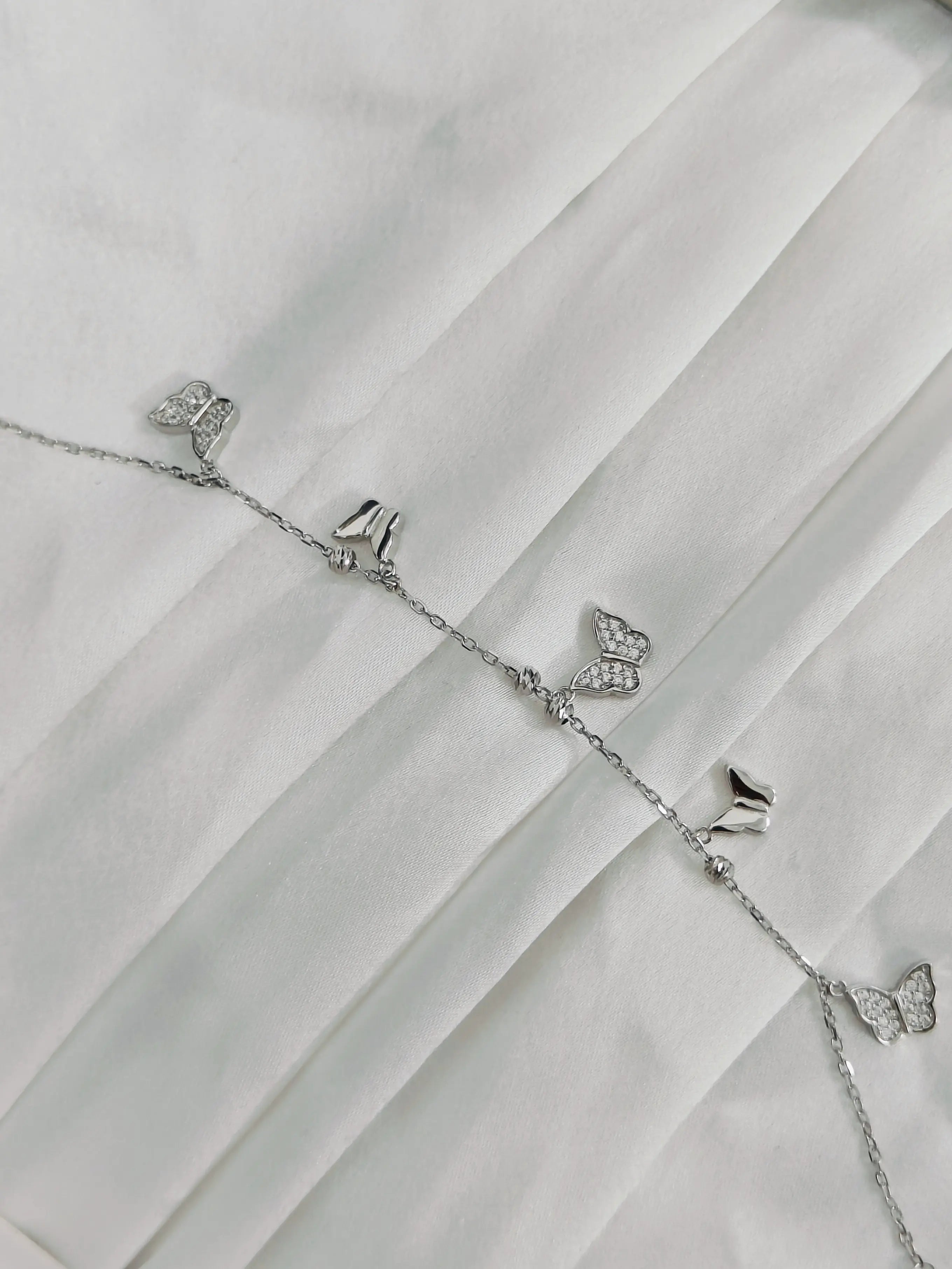 Silver butterfly charm bracelet on a white fabric background