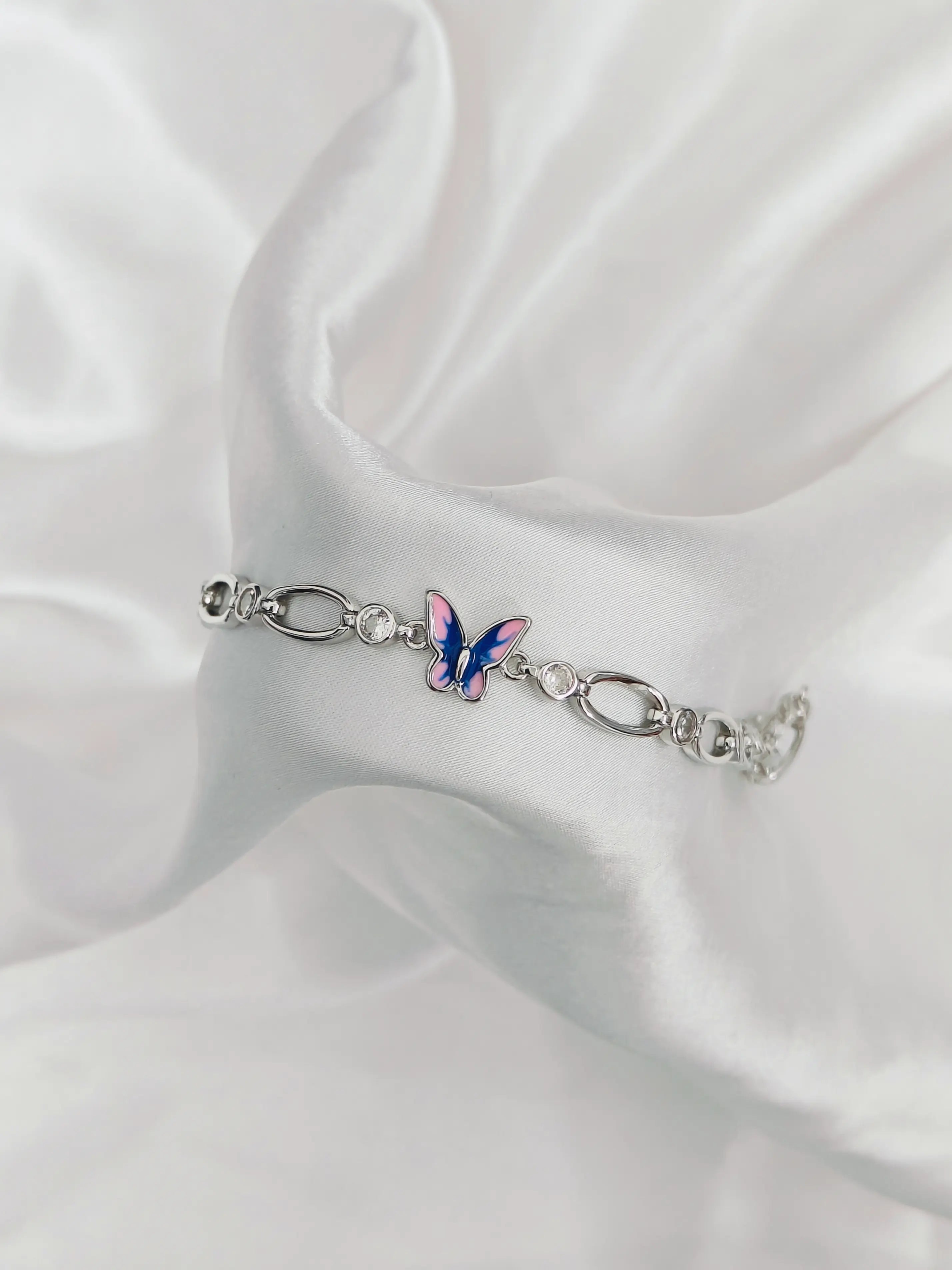Silver bracelet with a butterfly charm on a white fabric background