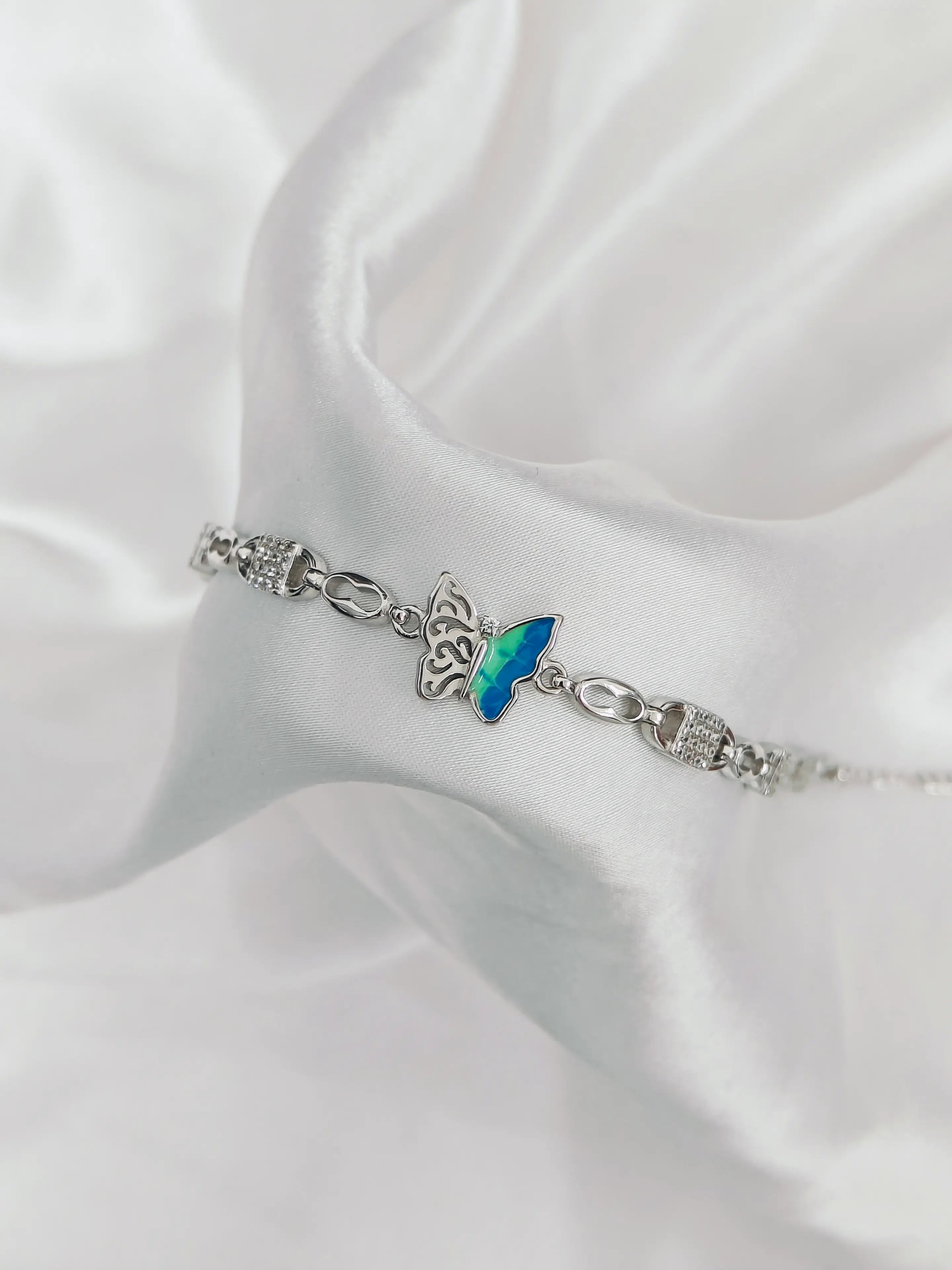 Silver bracelet with a blue butterfly charm on a white satin background