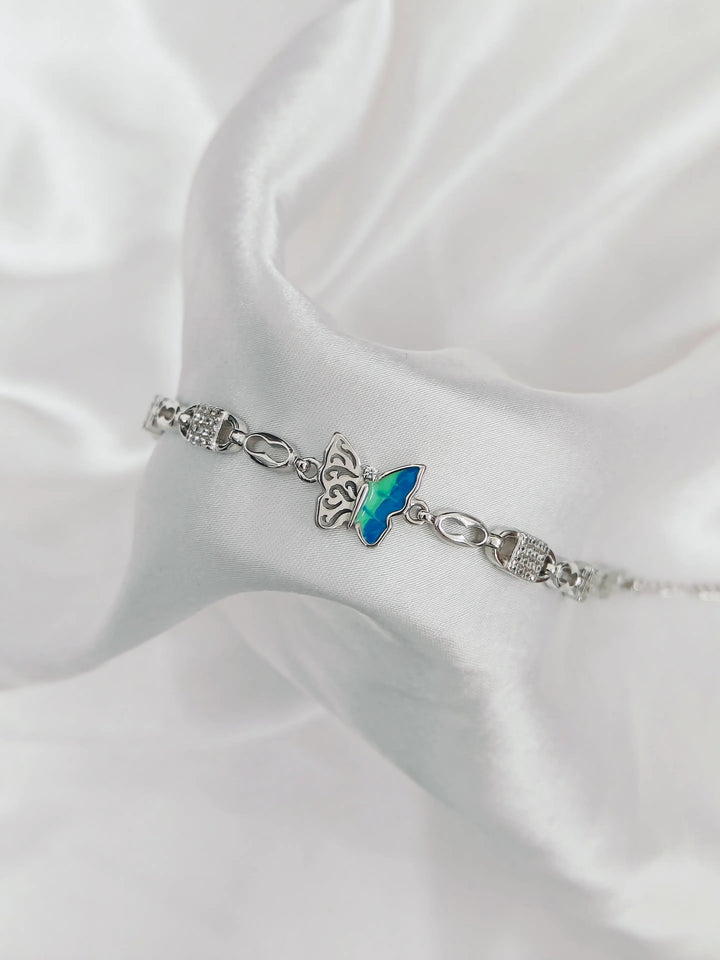 Silver bracelet with a blue butterfly charm on a white satin background