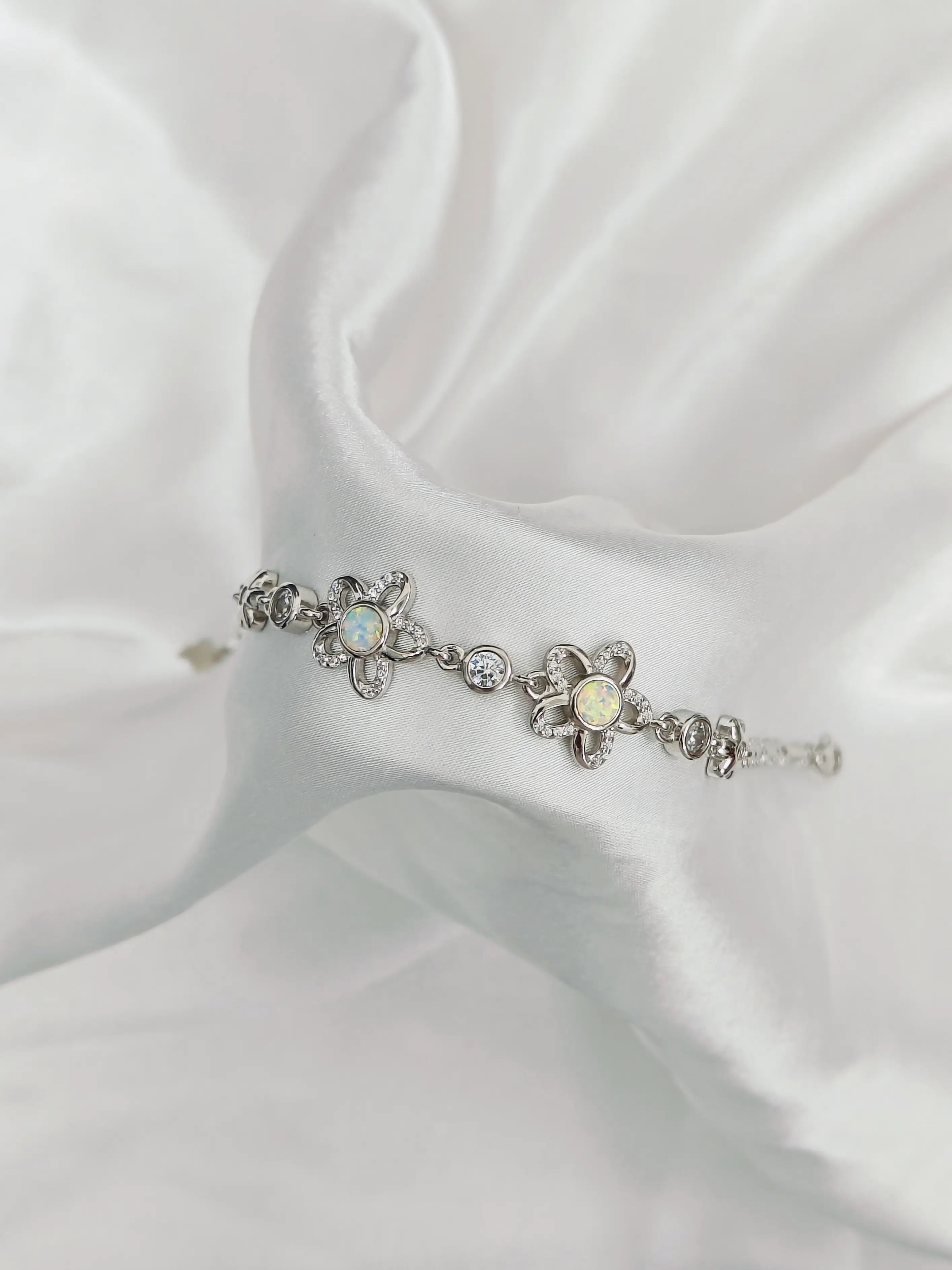 Silver bracelet with floral designs and gemstones on a white fabric background