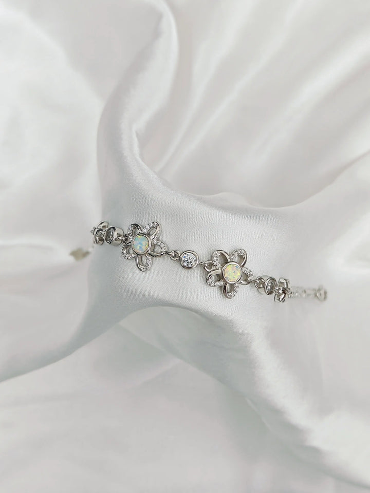 Silver bracelet with floral designs and gemstones on a white fabric background