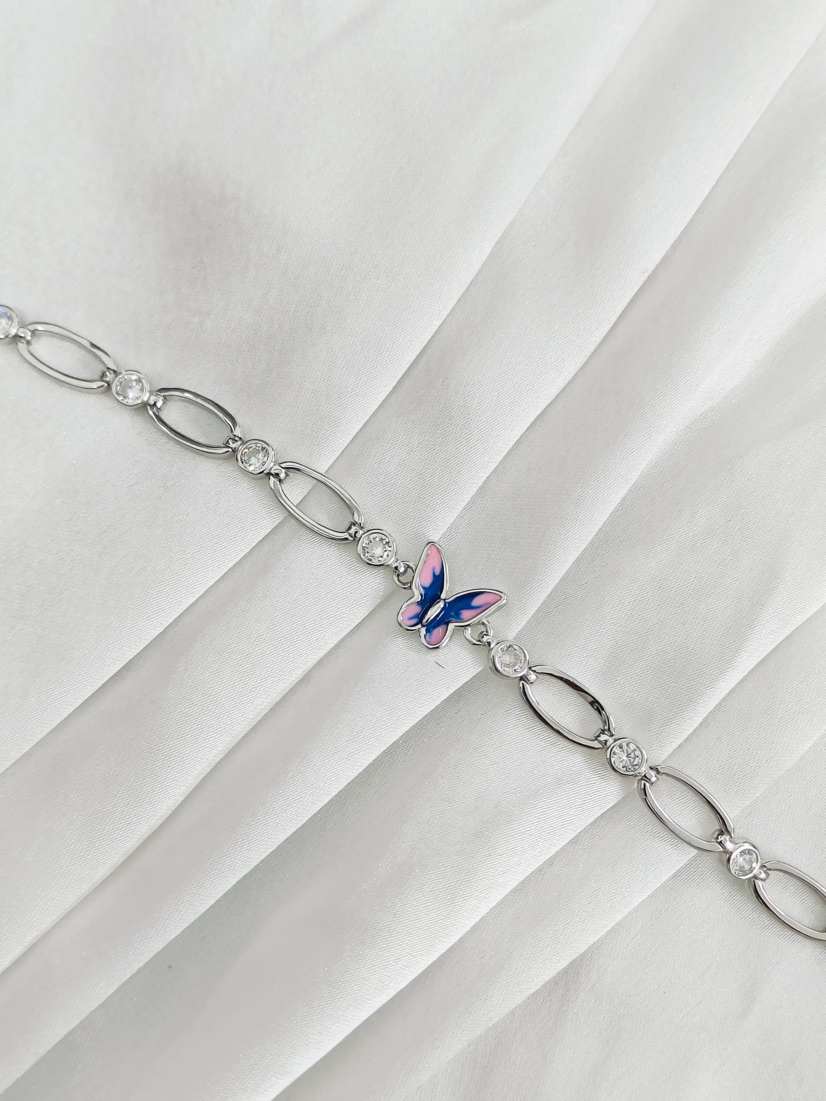 Silver chain bracelet with a butterfly charm on a white fabric background
