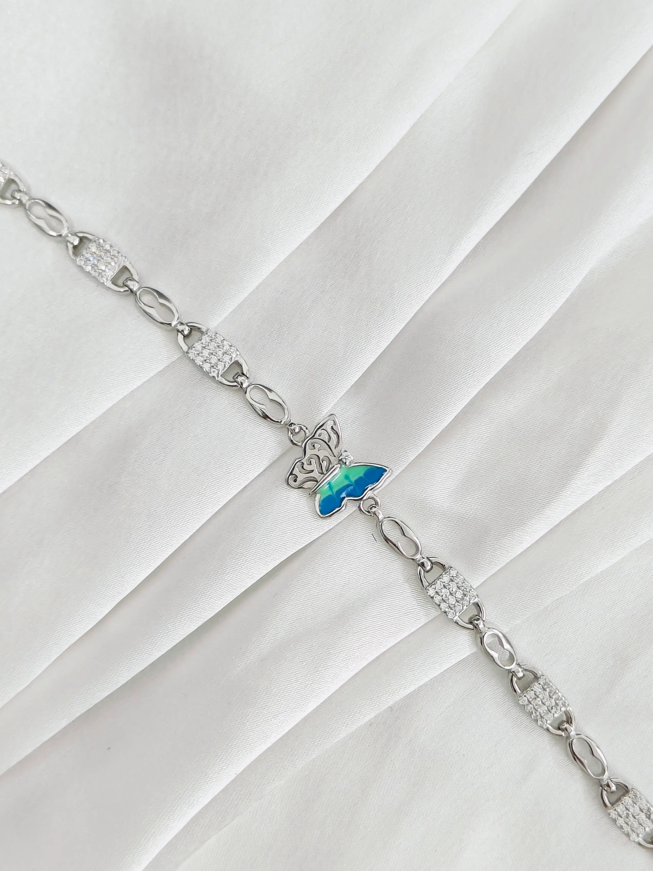 Silver bracelet with a butterfly charm on a white fabric background
