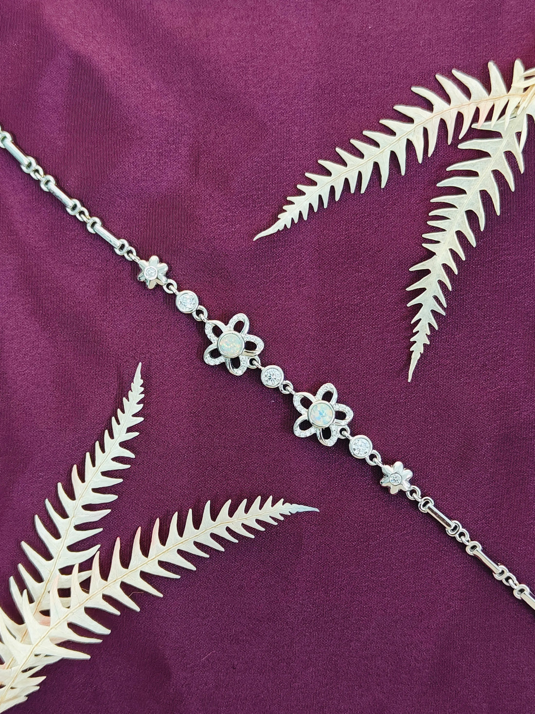 Silver chain necklace with floral designs on a purple fabric background
