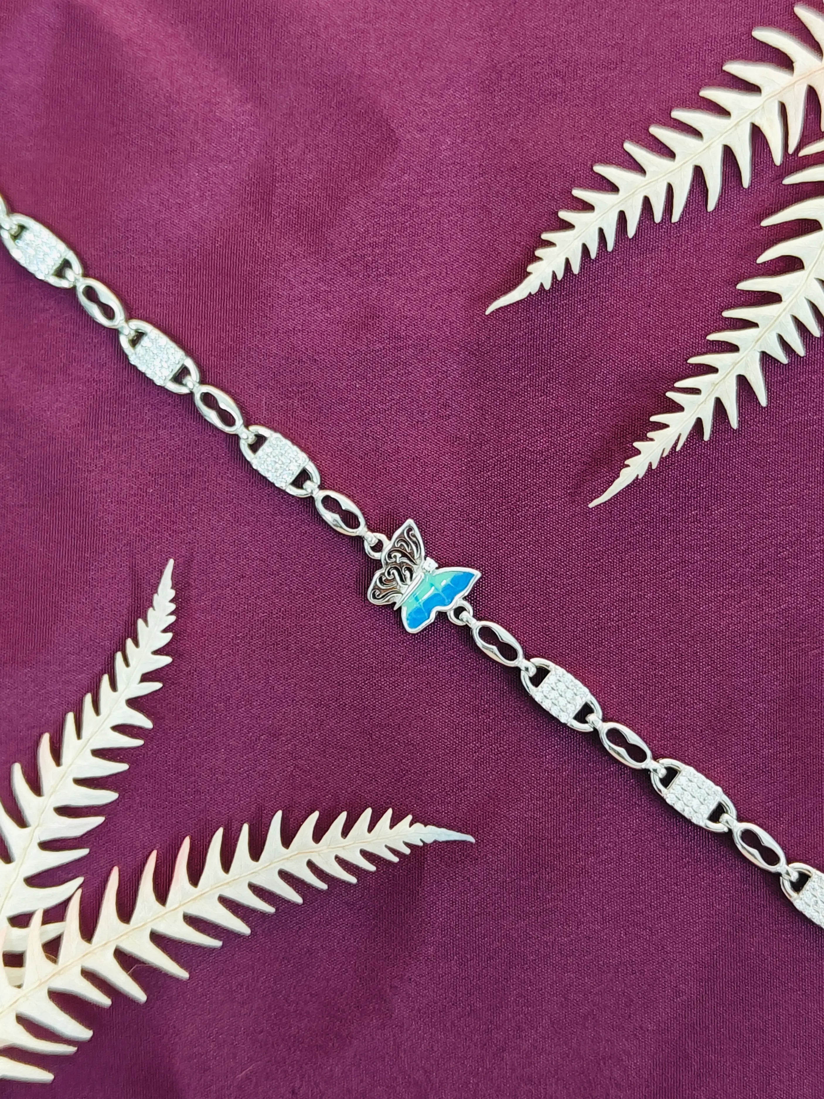 Silver bracelet with a butterfly charm on a purple fabric background with white leaves.